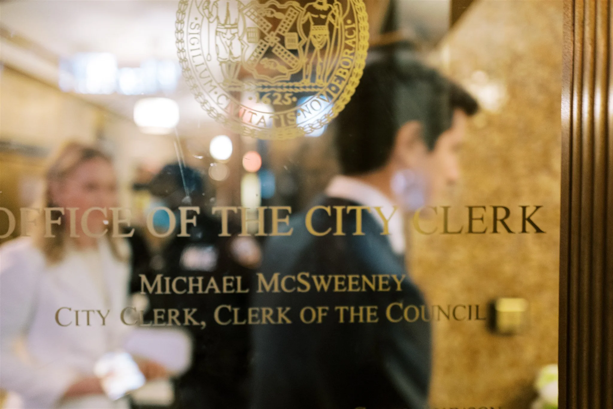 Gold lettering on the Office of the City Clerk door with the couple reflected in the glass. nyc city hall courthouse wedding photographer.