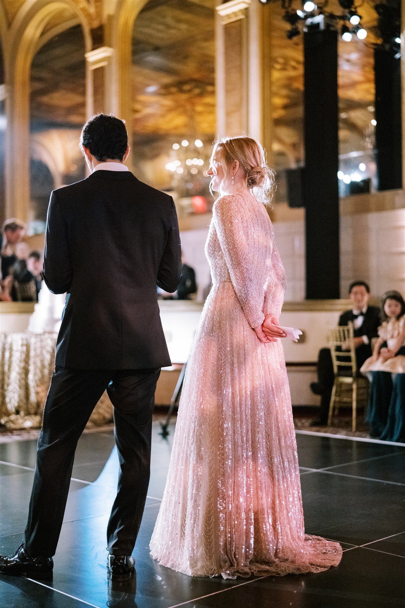 Bride and groom stand beneath golden arches listening to heartfelt speeches. luxury wedding planner michelle rago nyc.