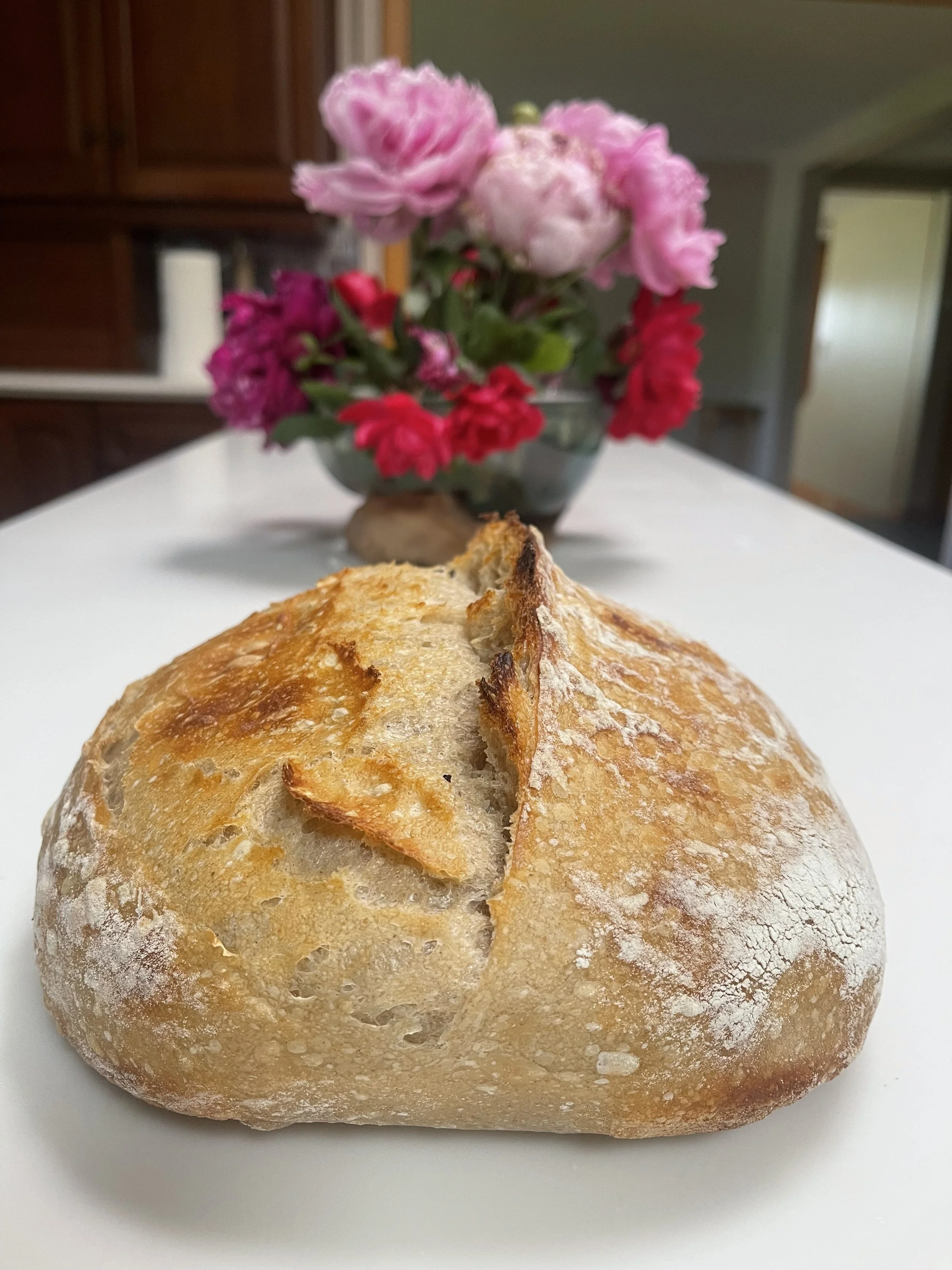A loaf of rustic sourdough bread on Pay10's Place counter alongside beautiful home grown florals in Newark, Oh.
