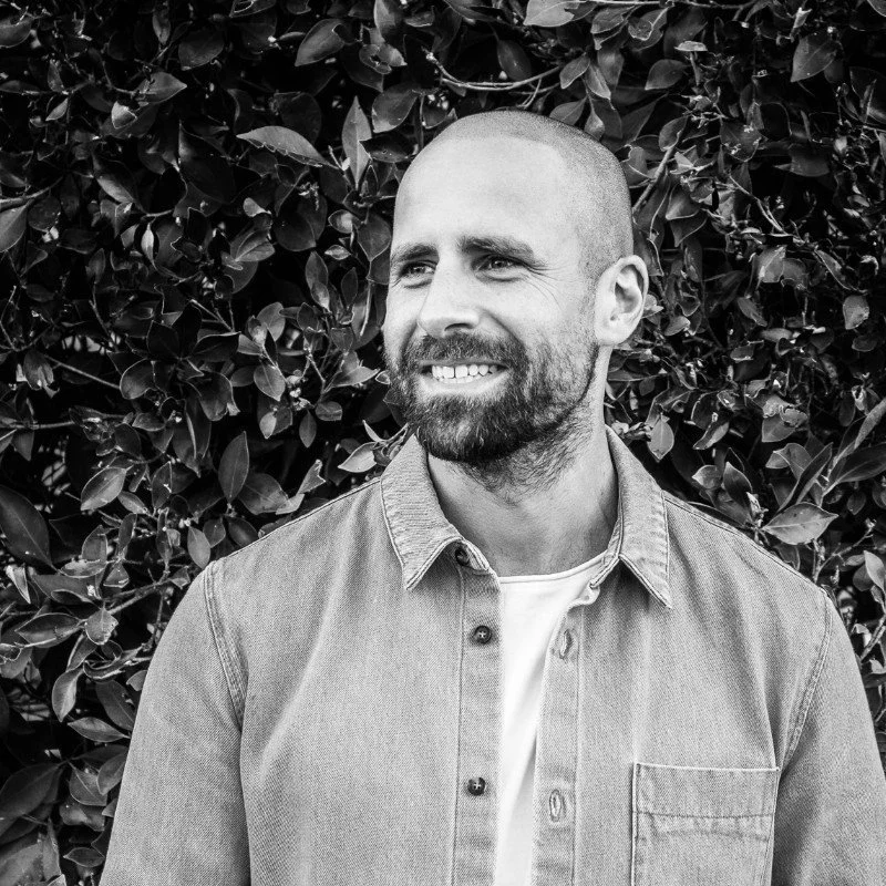 Man smiling in front of dense foliage, black and white photo.