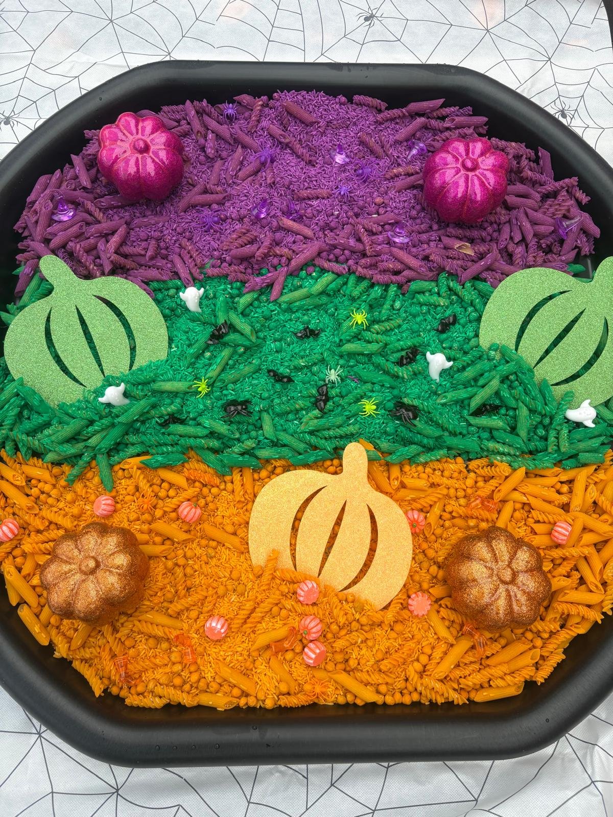 Halloween-themed sensory tray with purple, green and orange coloured rice, small pumpkins and themed accessories for toddler play.
