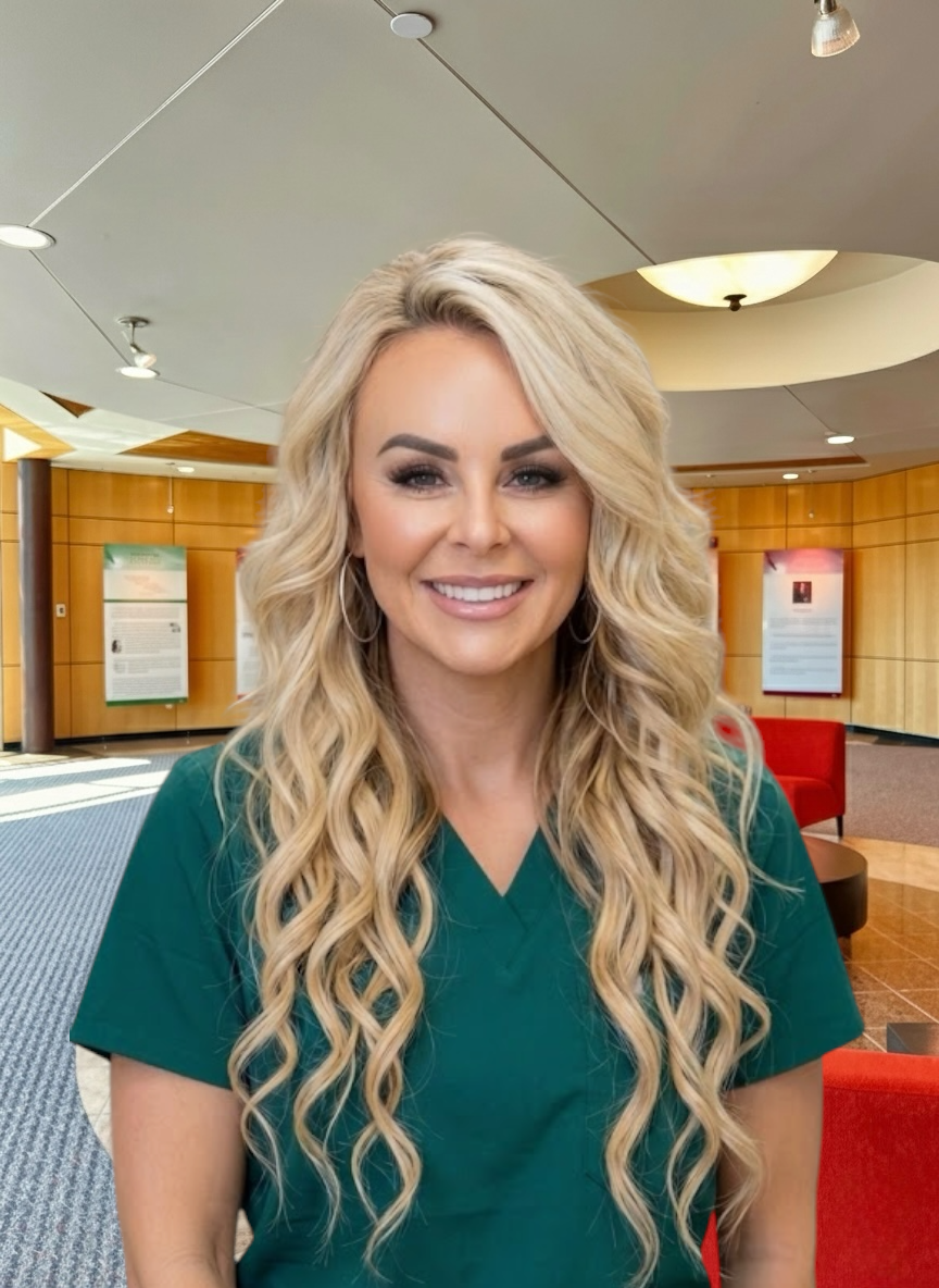 Portrait of a woman with curly dark hair, wearing purple scrubs and gold jewelry, smiling in an indoor setting.