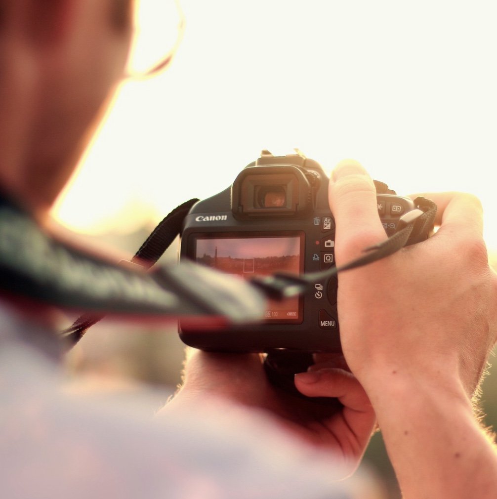A person holding a Canon camera and taking a photo of a sunset or sunrise.