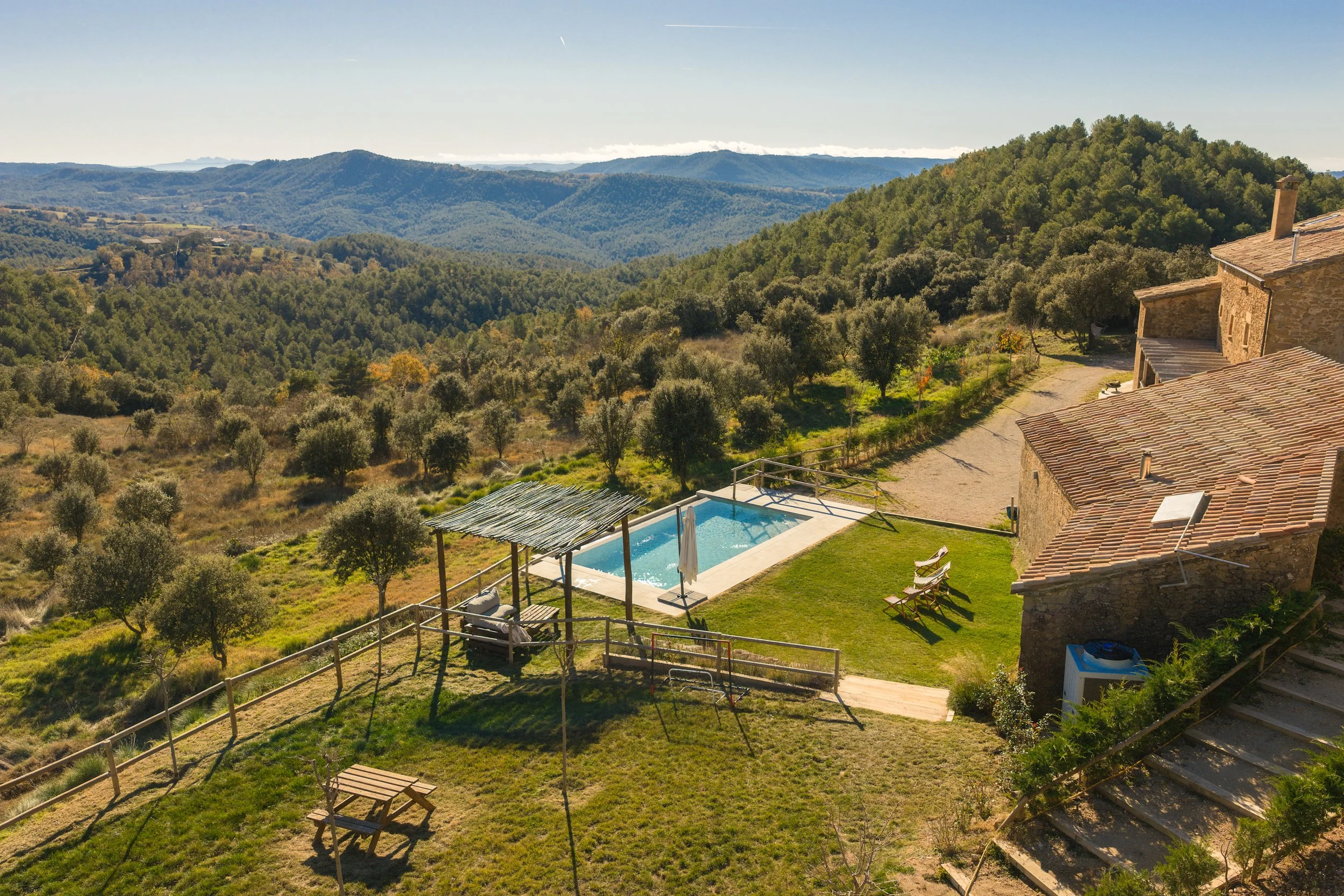 Villa rústica con piscina, áreas verdes, y vistas a colinas y bosques en un paisaje montañoso.