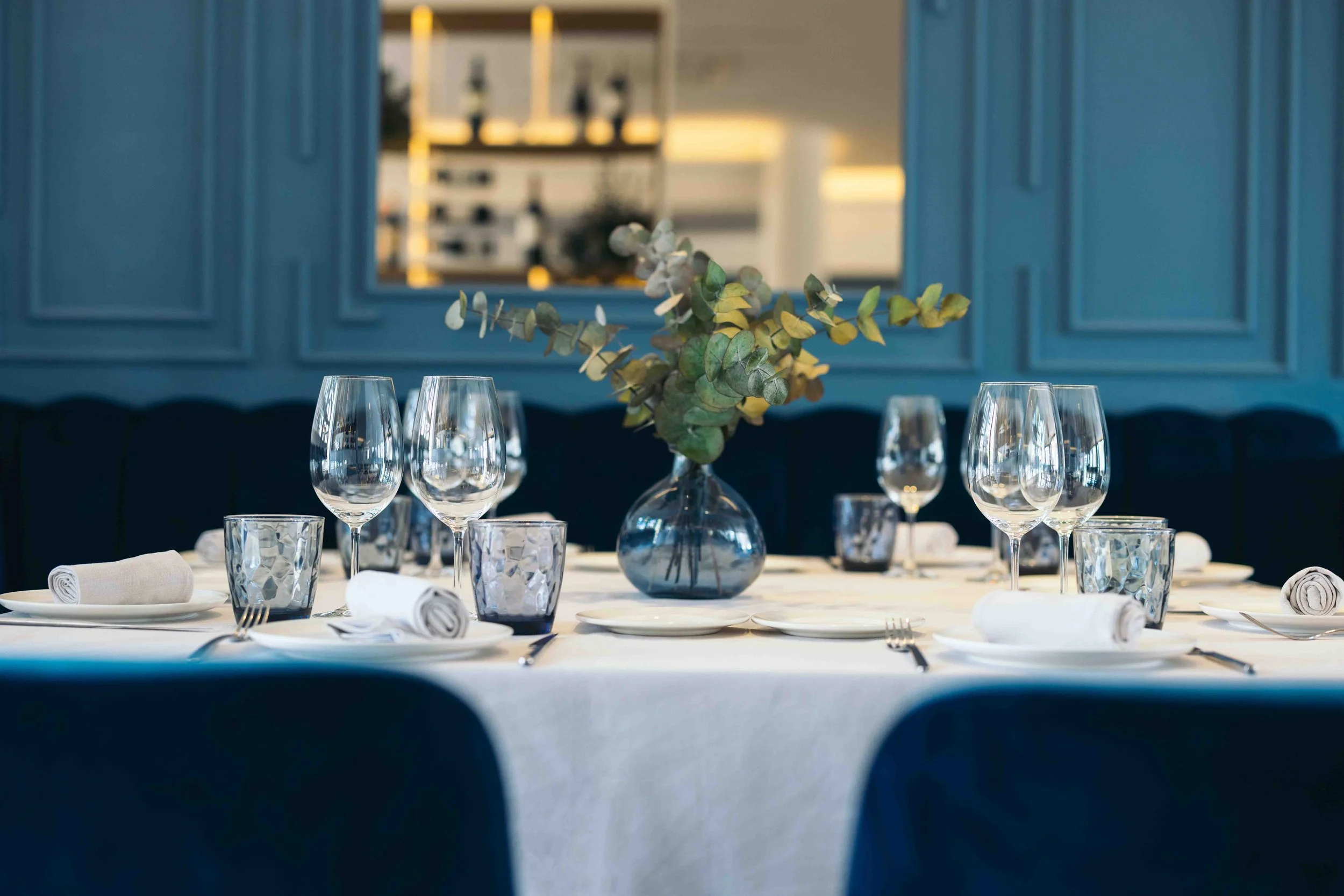 Mesa decorada con copas de vino, vasos y platos, con un centro de flores en un restaurante elegante.