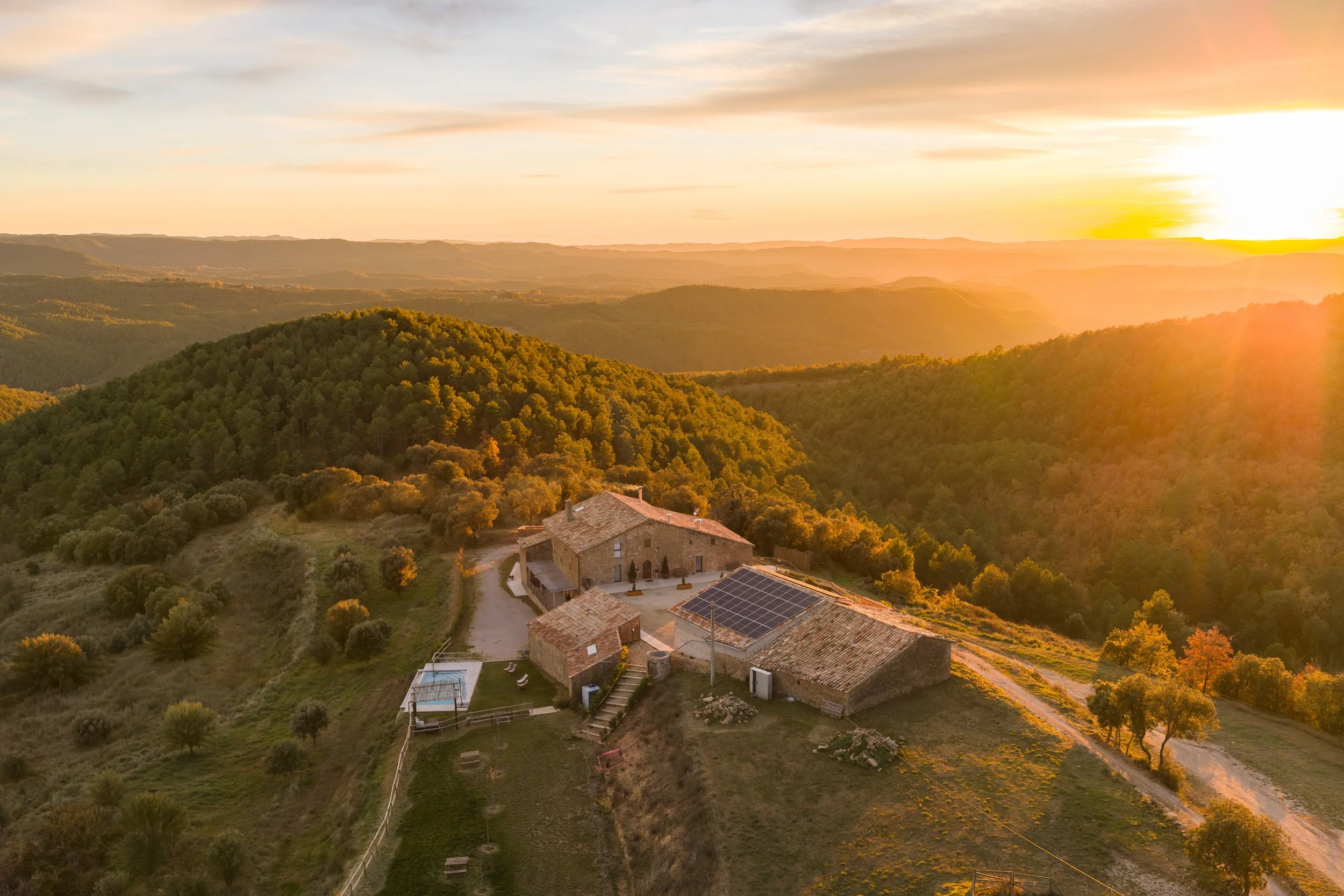 Paisaje rural con colinas y casas, al atardecer, con árboles y vegetación.