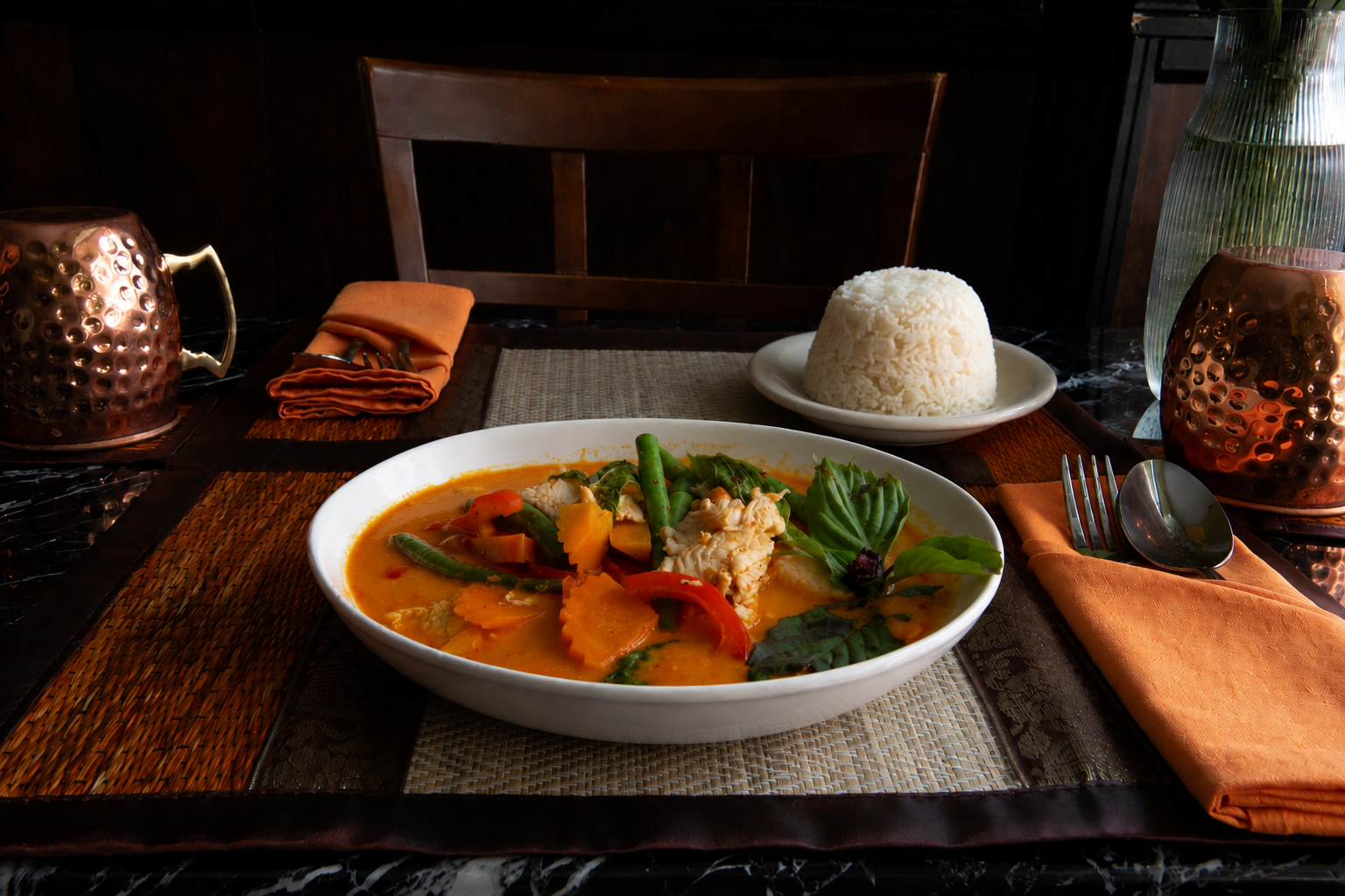 A white bowl of chili con carne with green peppers and a chili pepper on a wooden board, with chopped green onions and other chili dishes in the background.