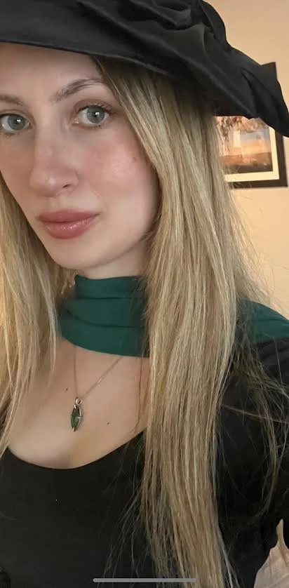 A woman smiling and hugging a black dog in a forest during fall.