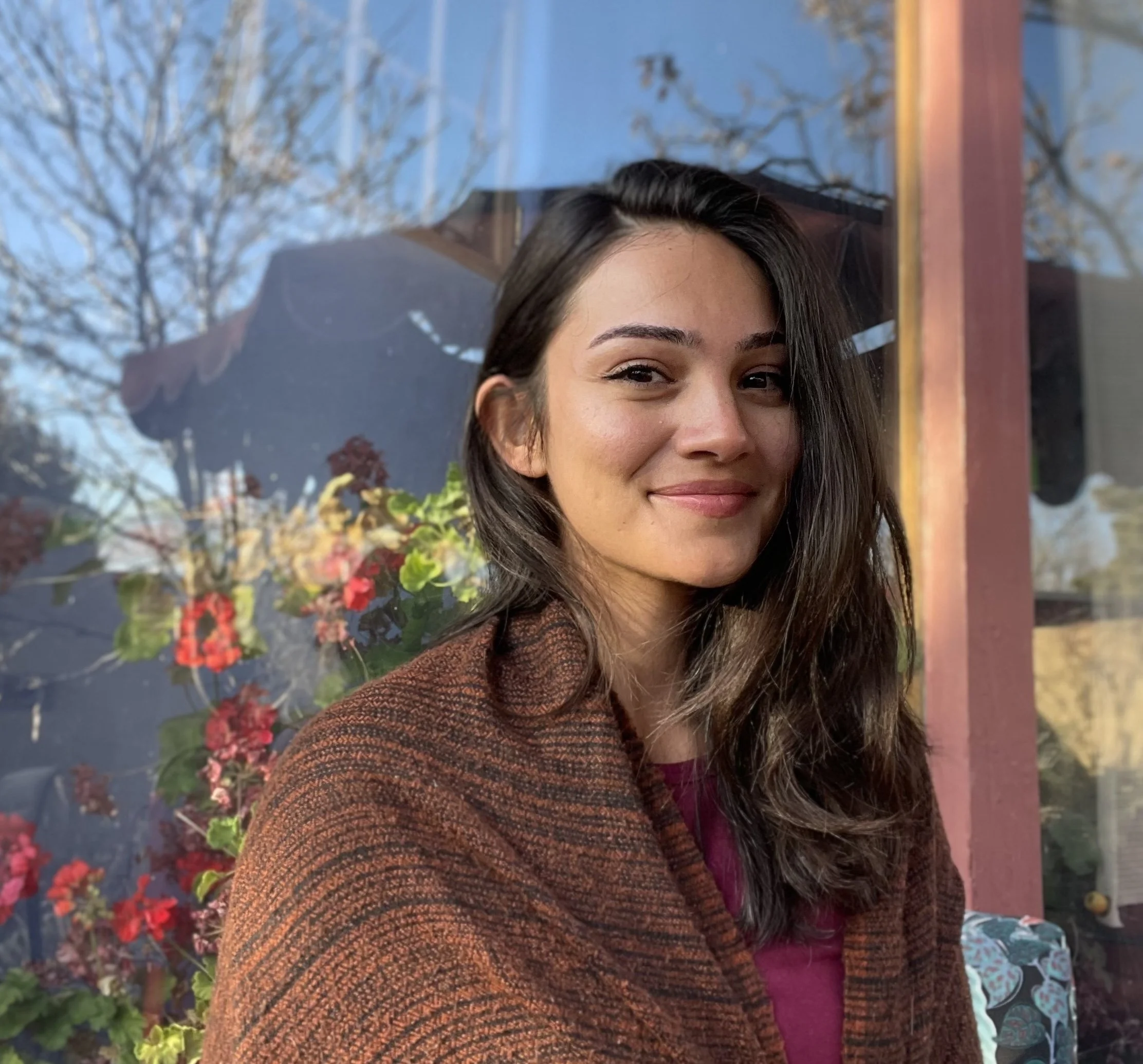 Woman sitting cross-legged in meditation pose, wearing white clothing and a white headwrap, with a large round mirror behind her, and meditation items around her.