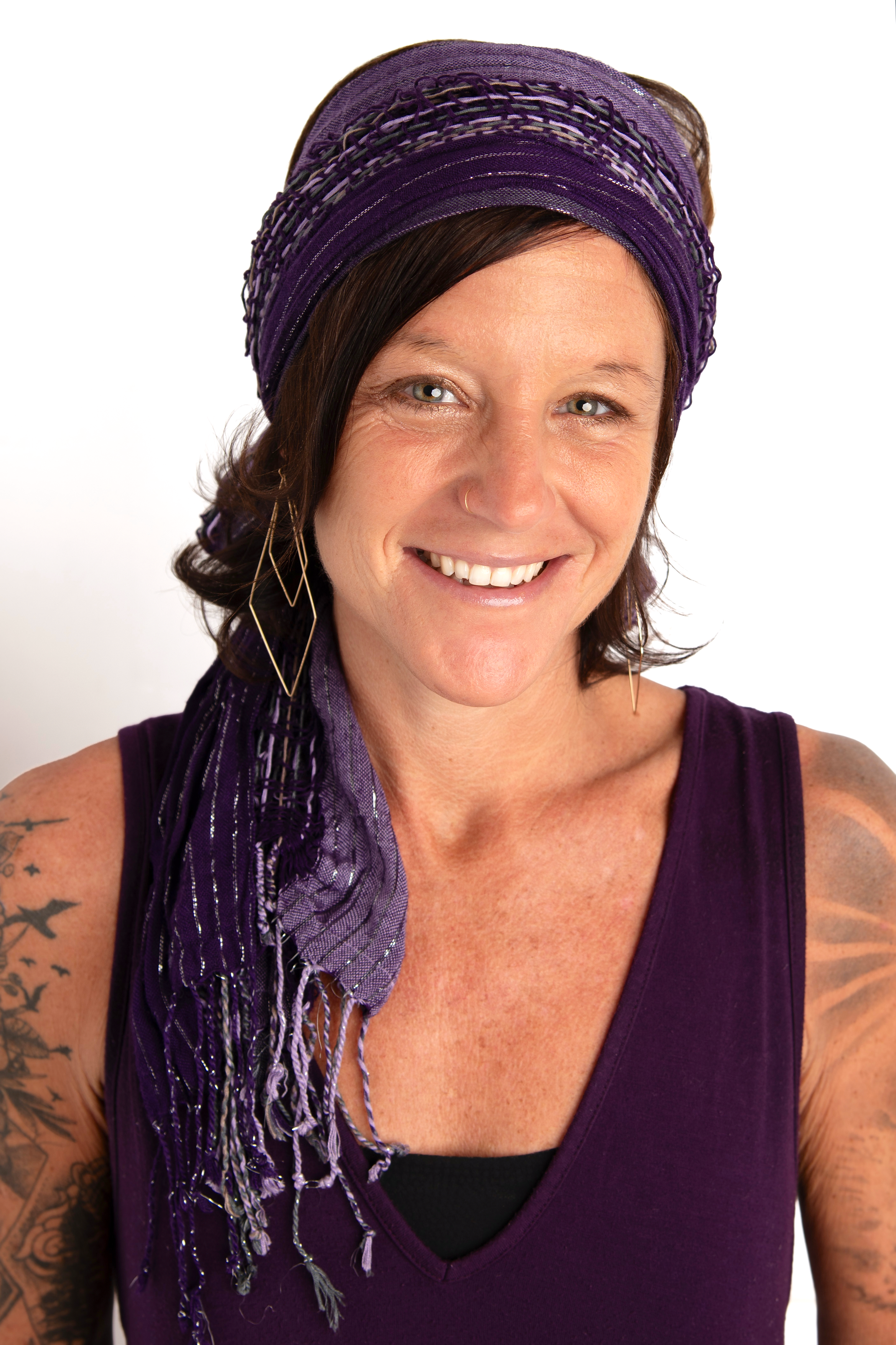 A person stands outdoors on a balcony with mountain scenery in the background. They are wearing a patterned shirt, black shorts, sandals, and glasses, and are standing next to a drum with a furry cover.