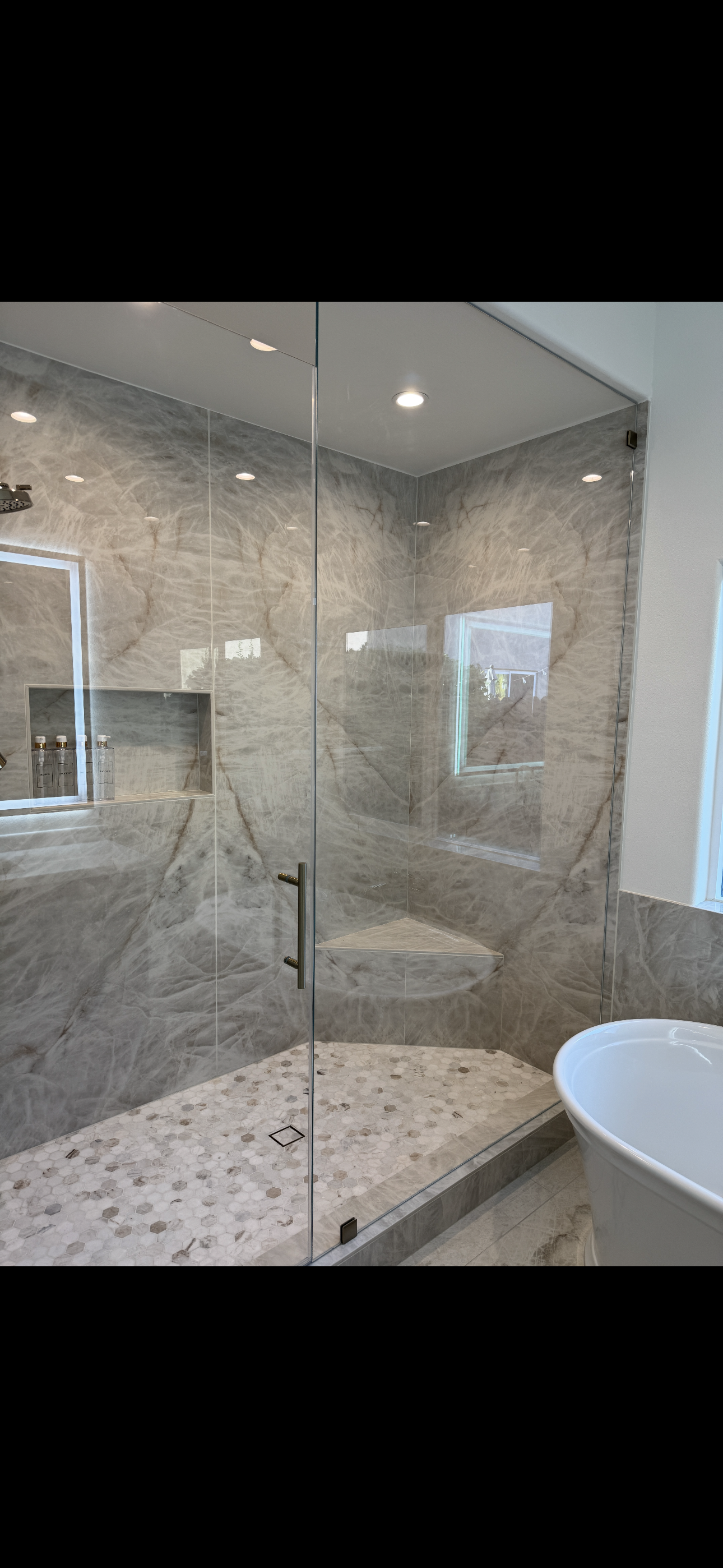 Luxurious bathroom remodel featuring a large glass-enclosed shower with marble tile walls, built-in bench seating, recessed lighting, and a modern freestanding tub by Sam’s Renovations & Home Improvements.