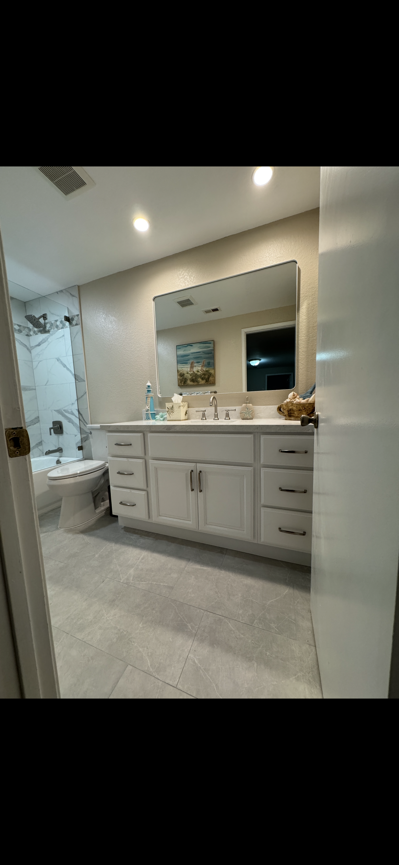 Bright modern bathroom remodel featuring a white double vanity with quartz countertop, large illuminated mirror, recessed lighting, and updated tile flooring by Sam’s Renovations & Home Improvements.