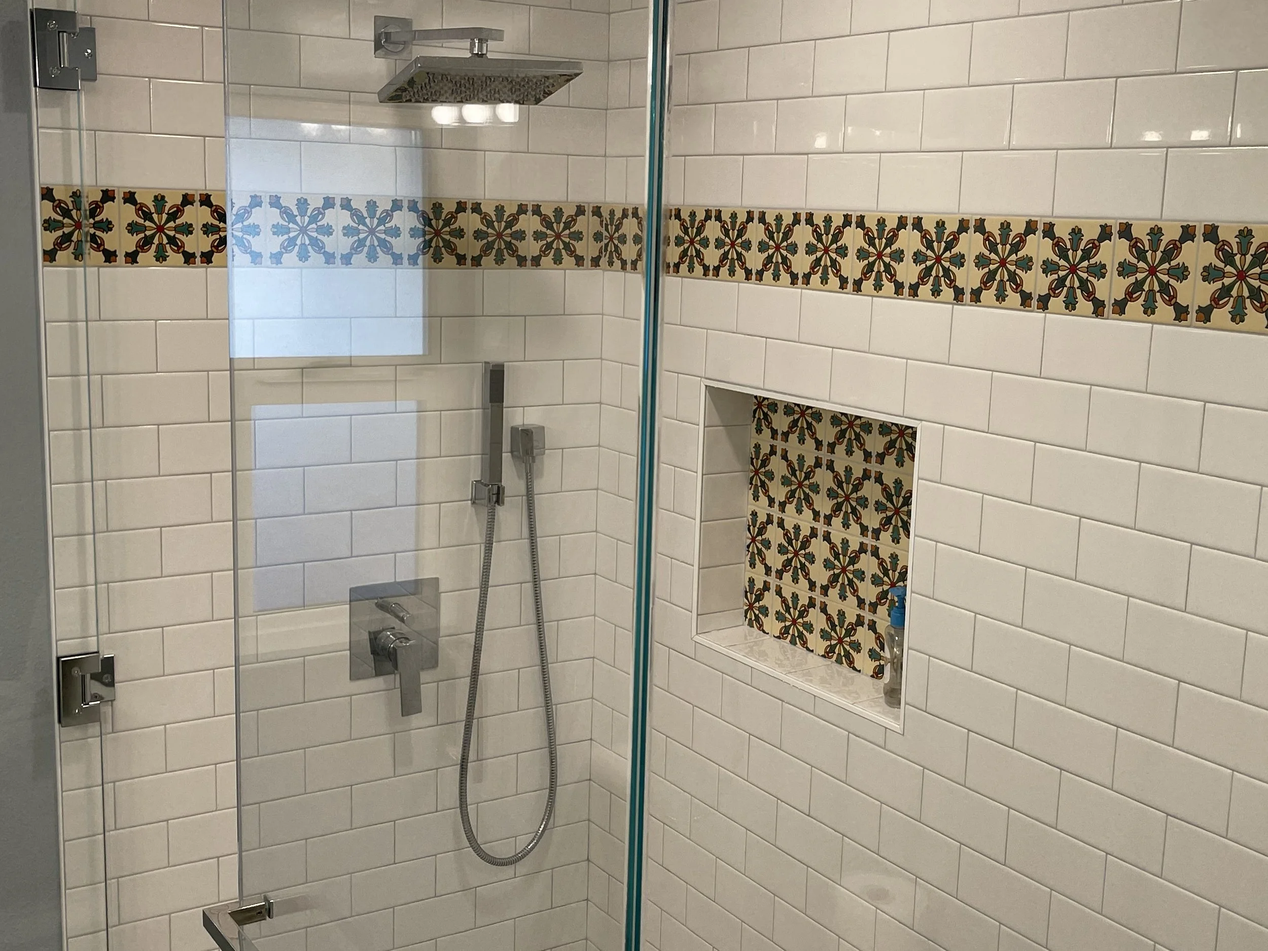 White subway tile shower with decorative Spanish-style accent tile band, matching niche detail, and modern chrome fixtures by Sam’s Renovations & Home Improvements.