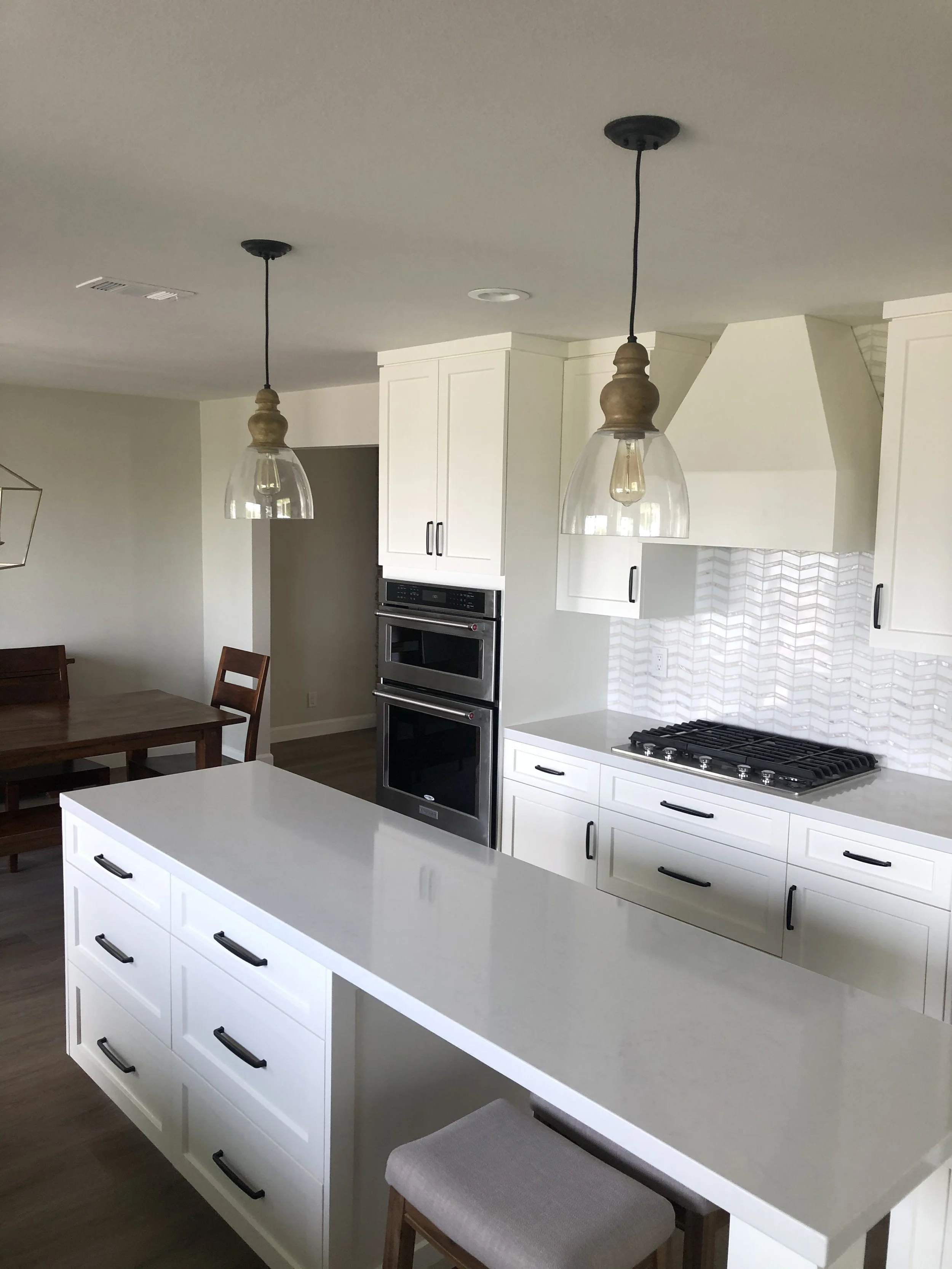Bright modern kitchen remodel featuring white shaker cabinets, quartz countertops, stainless steel double ovens, gas cooktop, and chevron tile backsplash completed by Sam’s Renovations & Home Improvements.