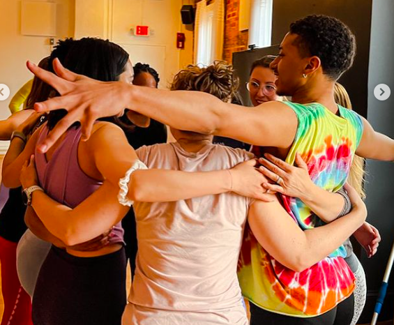 A group of diverse women hugging and embracing each other in a warm, celebratory moment inside a room.