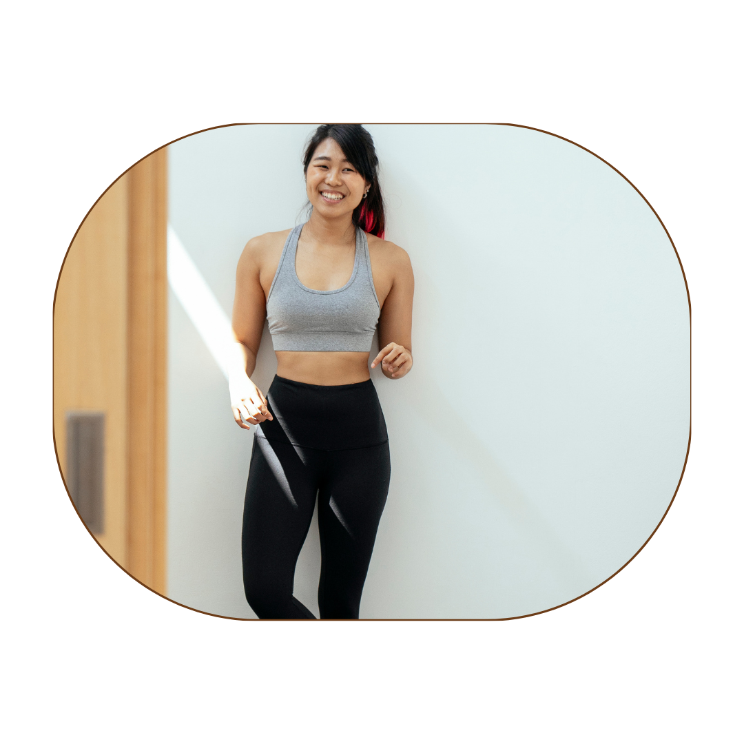 Young woman in workout clothes smiling and leaning against a white wall.
