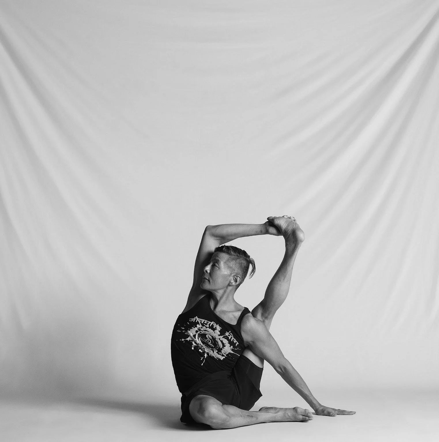A person practicing yoga in a seated twist pose on a white studio background.