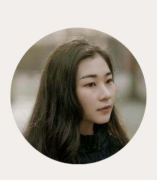 A young woman with long dark hair and fair skin, looking to the side, outdoors in a natural setting.