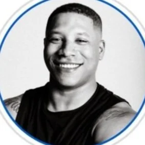 Black and white portrait of a smiling man with short hair, wearing a sleeveless shirt, against a plain background.