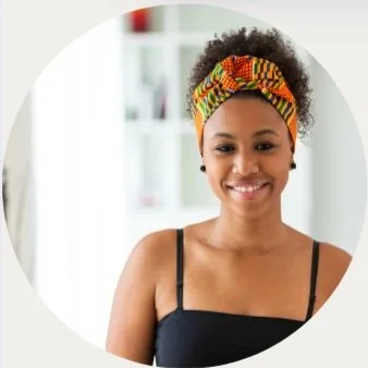 A young woman with a colorful headwrap smiling in a well-lit room.