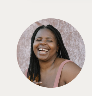 Smiling woman with long dreadlocks in front of a patterned wall