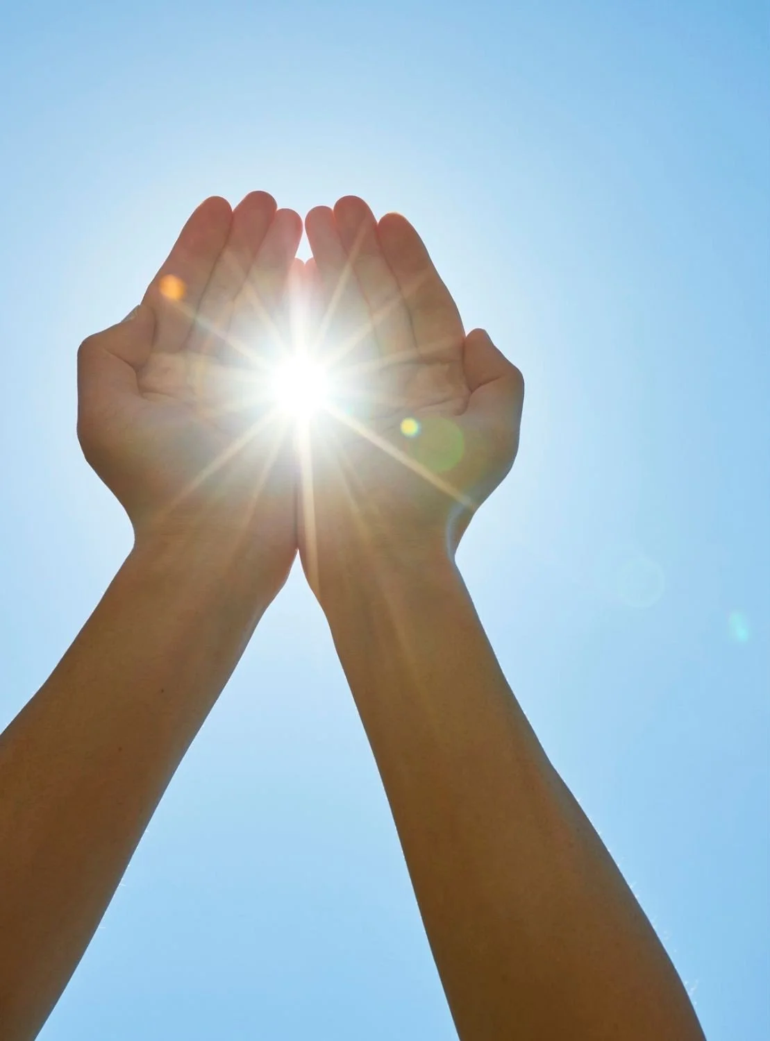 Two hands cupping the bright sun against a clear blue sky.