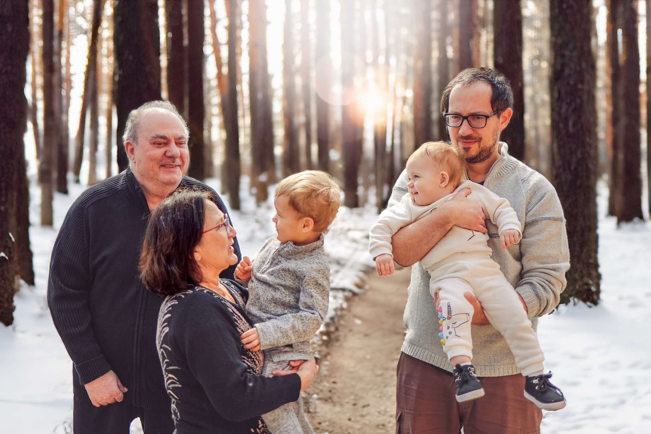 Family of four laughing outdoors in a snowy forest during sunset in Calgary, with two adults and two children, engaging in conversation and enjoying nature.
