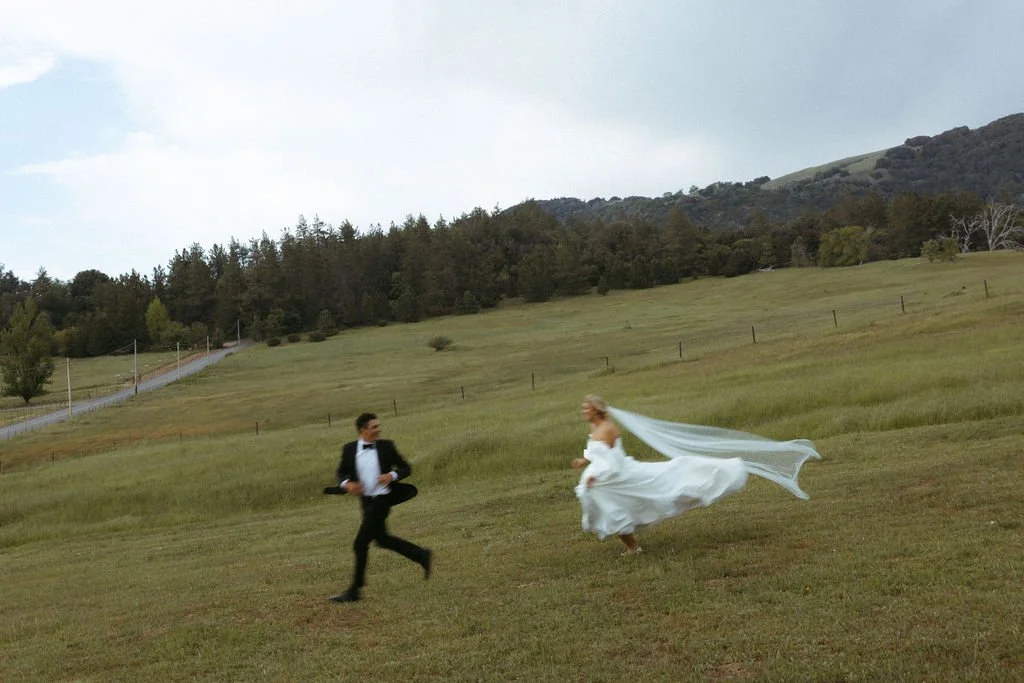Bride and groom run through open field in beautiful outdoor Southern California wedding venue