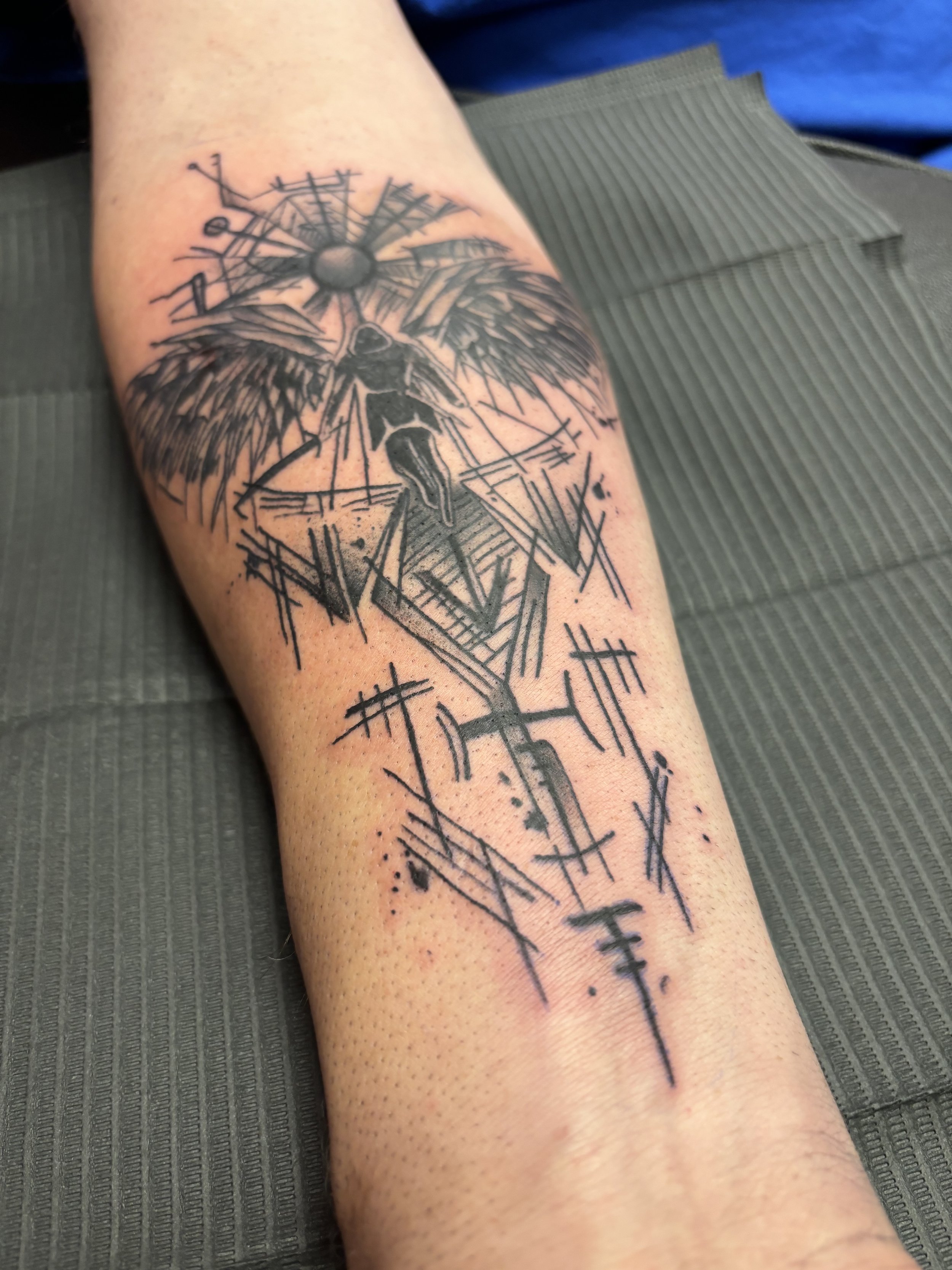 Black ink tattoo of an angel with large wings and a sword, with abstract and geometric elements surrounding it.