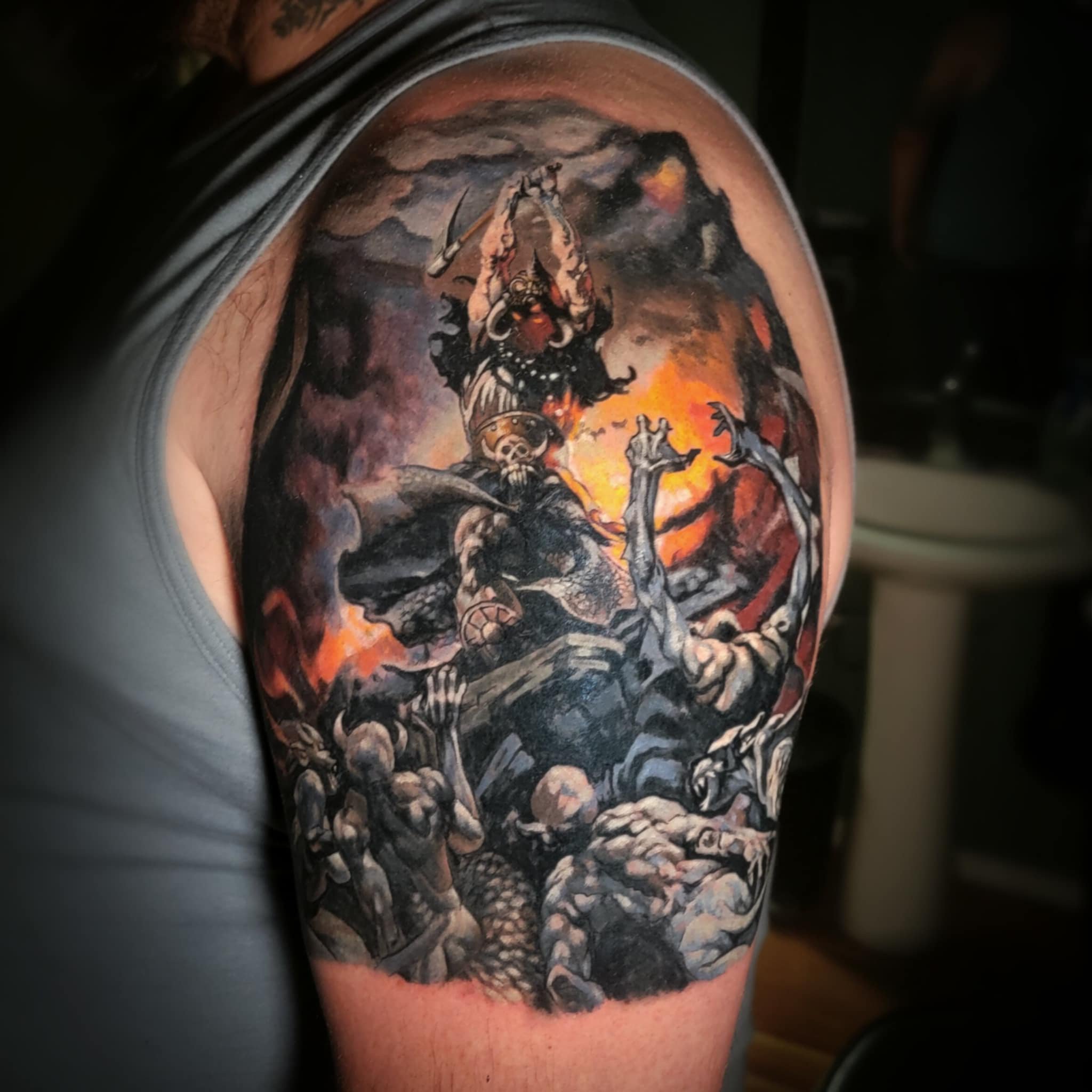A detailed black and gray and color tattoo depicting a fierce warrior battling a demon, with a fiery background and various mythological figures and monsters.