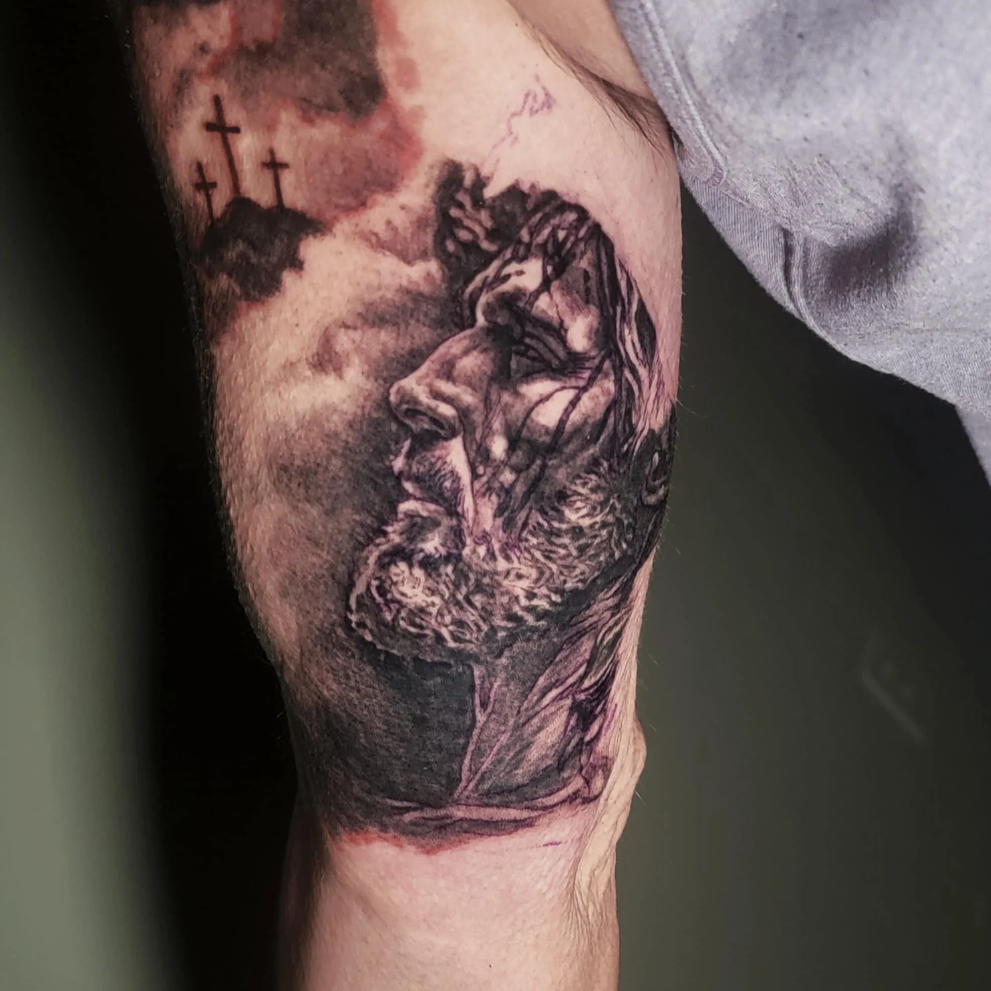 Tattoo of a crying Jesus Christ with three crosses on a hill in the background