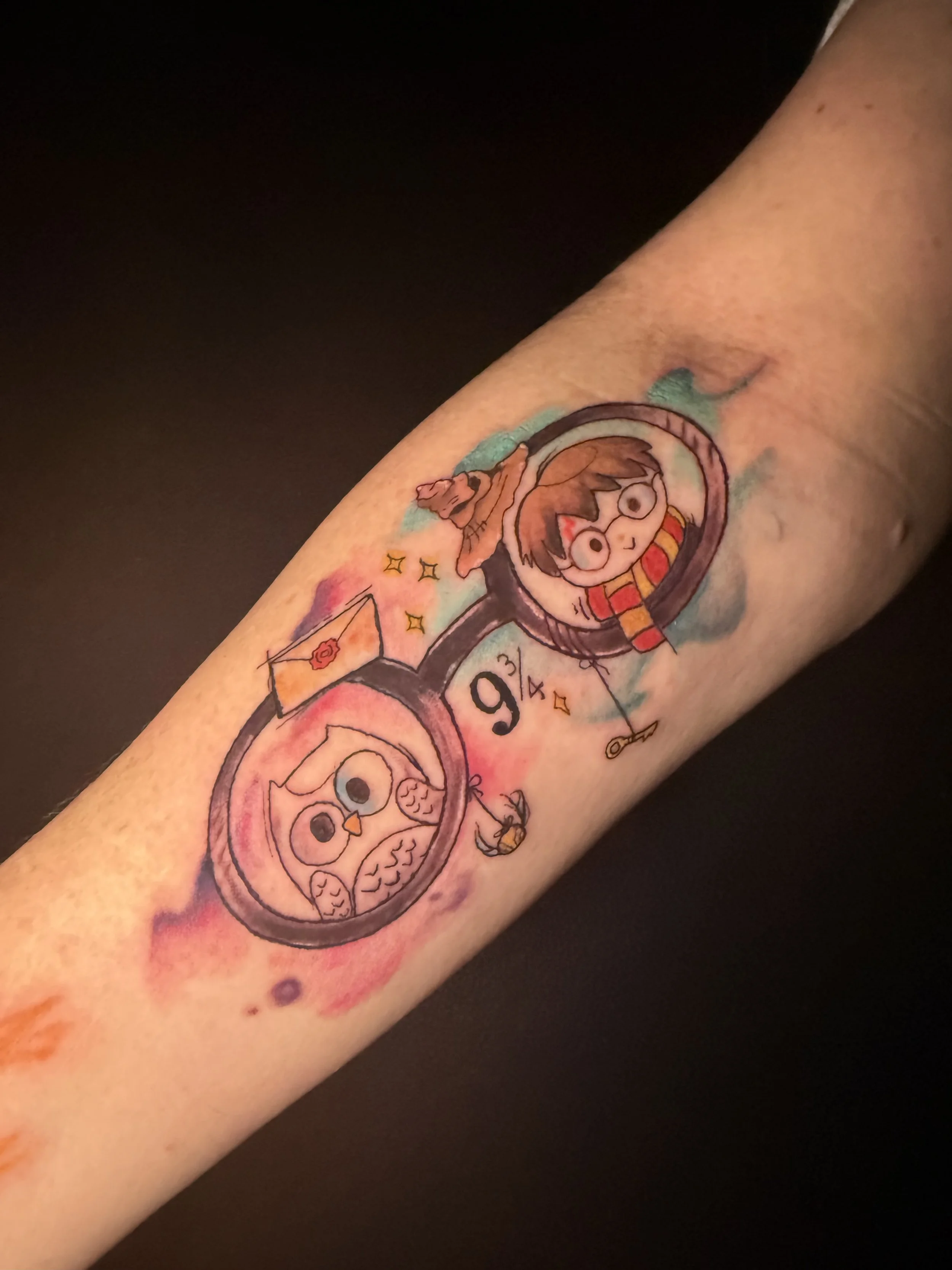 Watercolor tattoo of a pair of round glasses with cartoon characters, one with glasses and a red scarf, and an owl, surrounded by small details and colorful splashes.