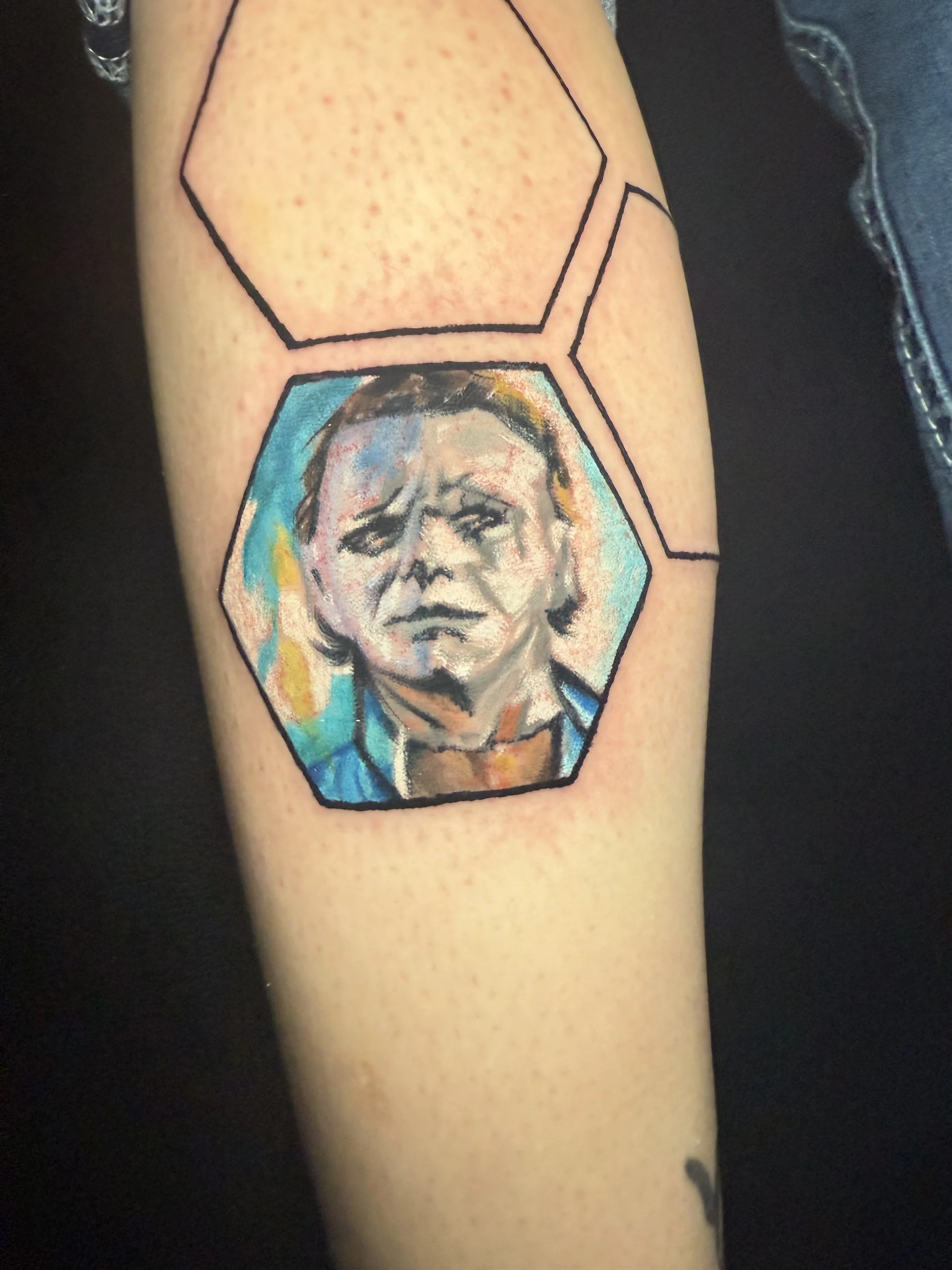 Tattoo of a child's portrait inside a hexagon with watercolor style background on a person's arm.