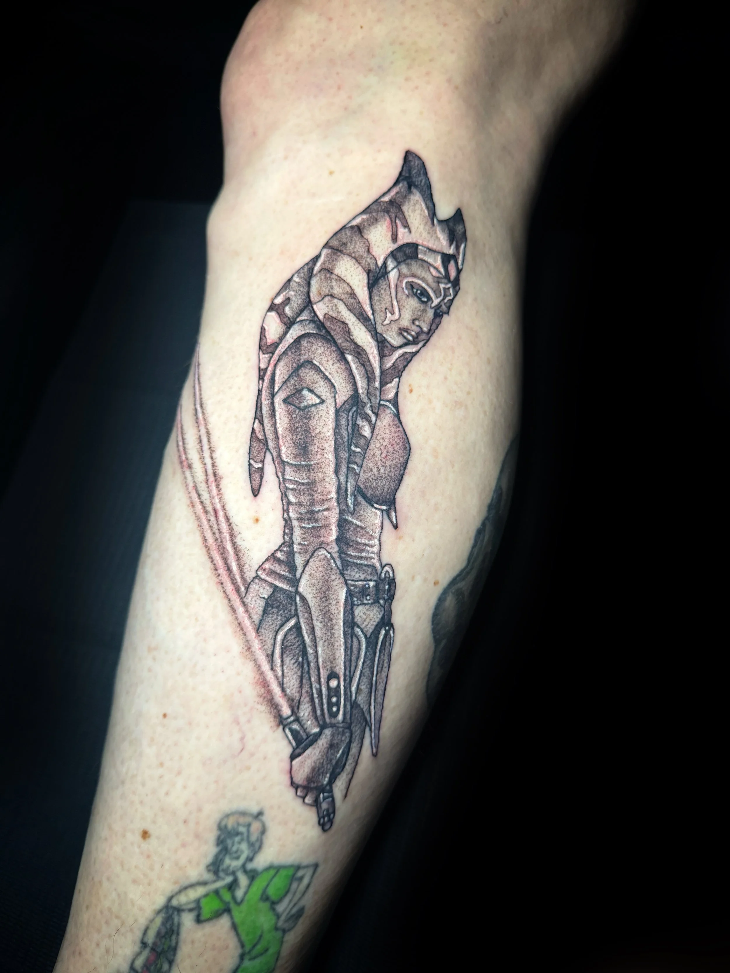 Tattoo of a female character with dreadlocks, dressed in futuristic armor, holding a sword, in black and gray ink on person's arm.