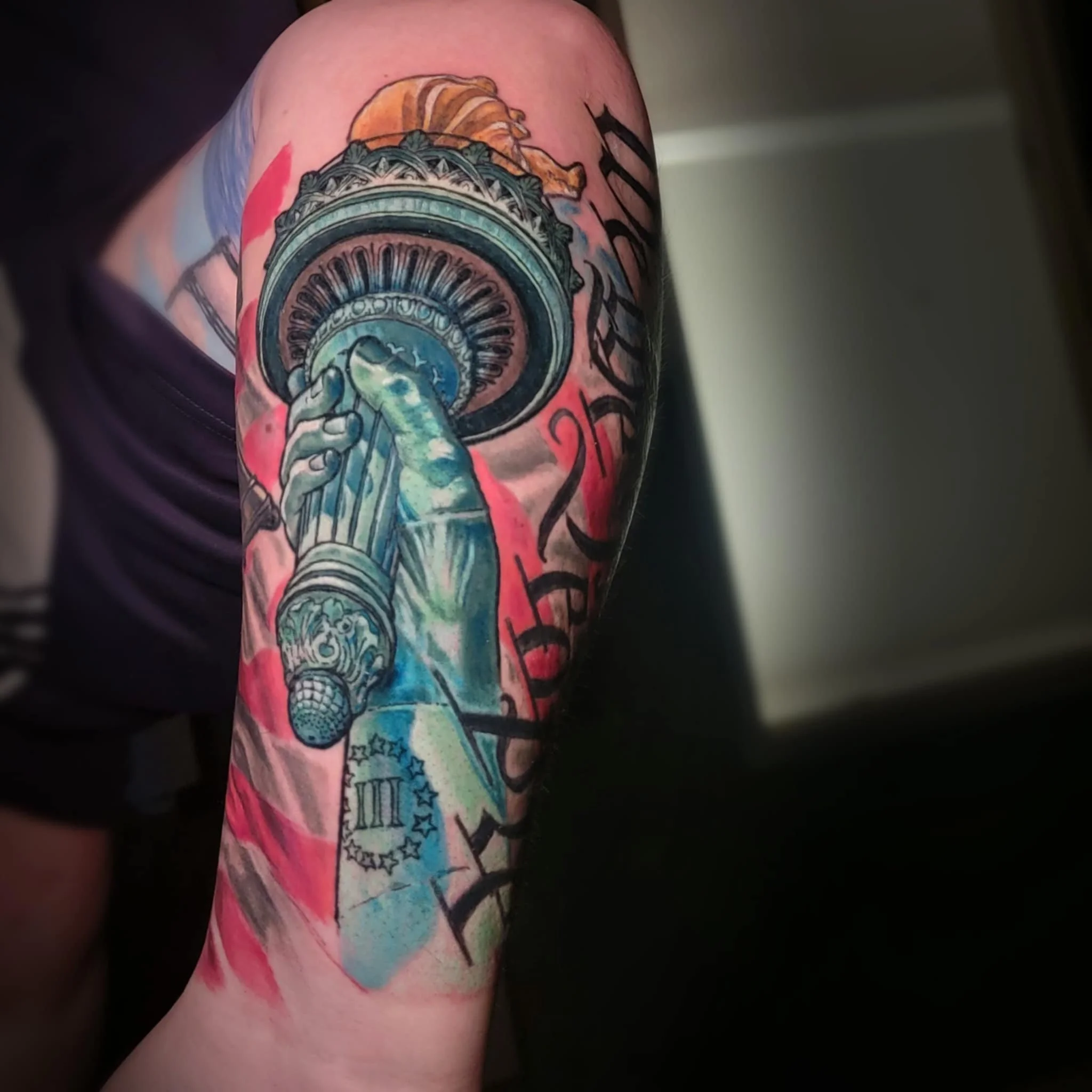 Colorful tattoo of a statue of liberty's torch with American and European union flags and decorative elements on an arm.