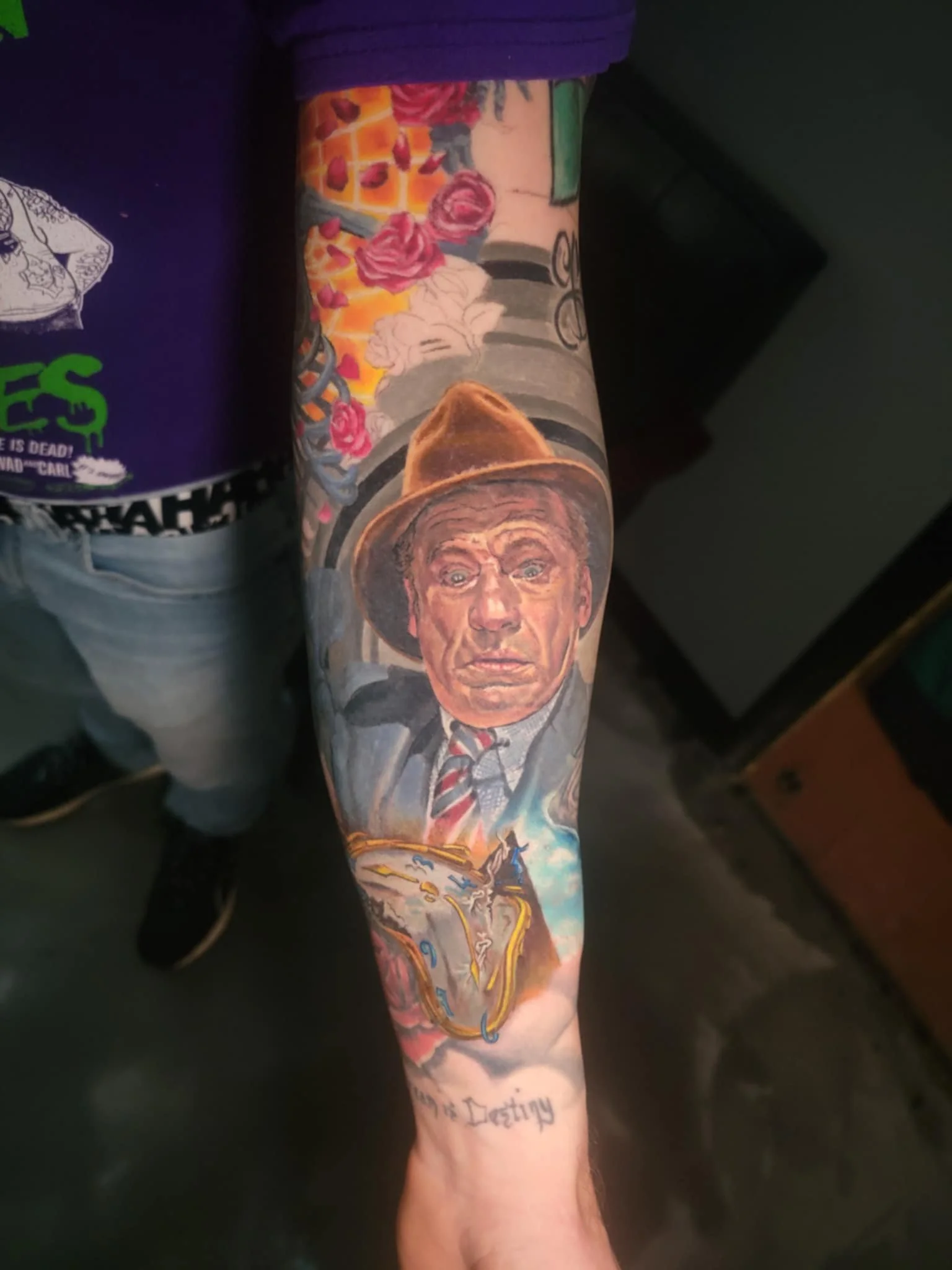 Colorful tattoo sleeve featuring a portrait of a man wearing a hat, a train, flowers, and clouds, with the phrase 'In the Destroiy' below.