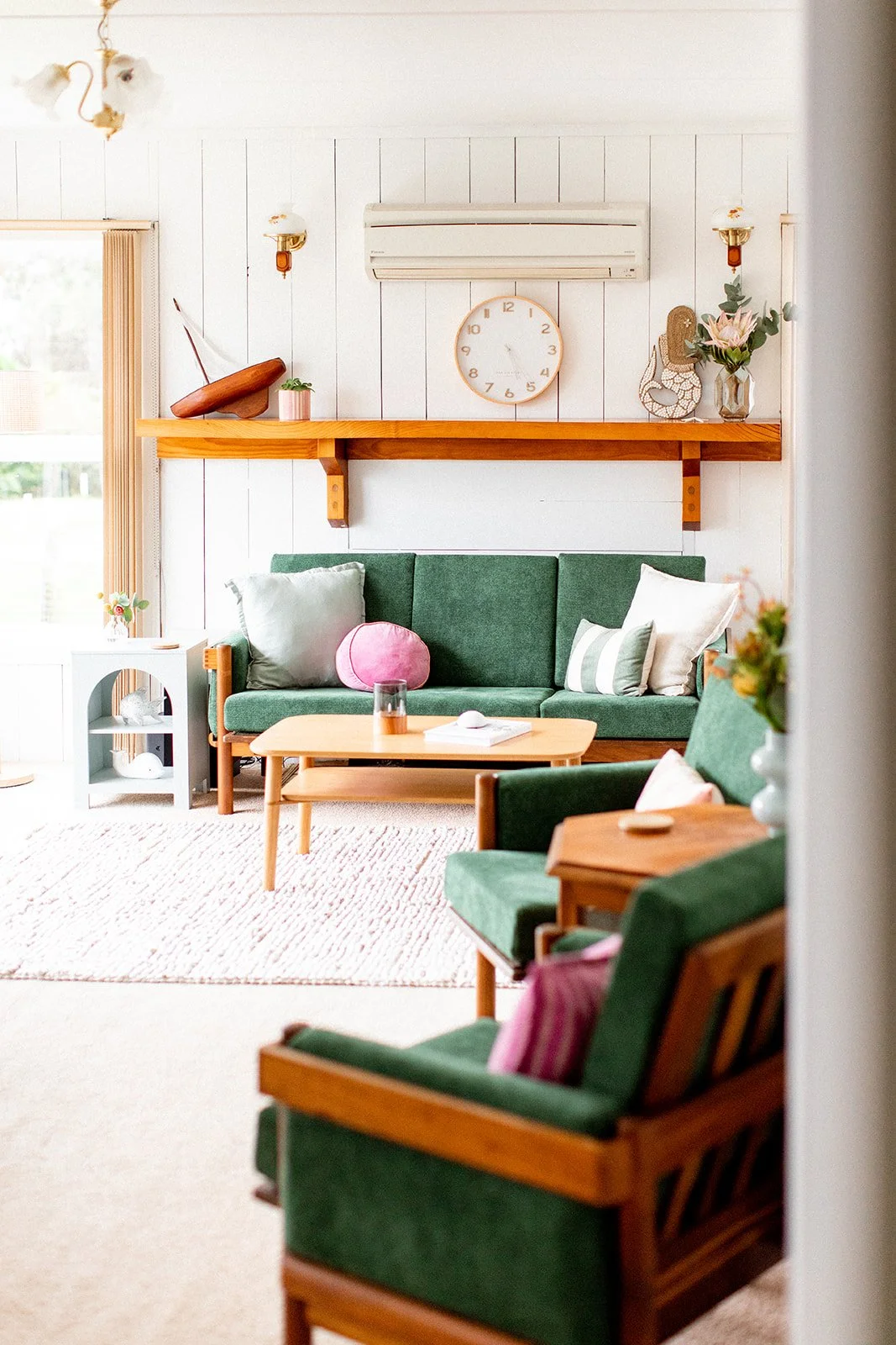 Cozy living room with green sofas, wooden coffee table, a wall clock, and decorative items on a wooden shelf.