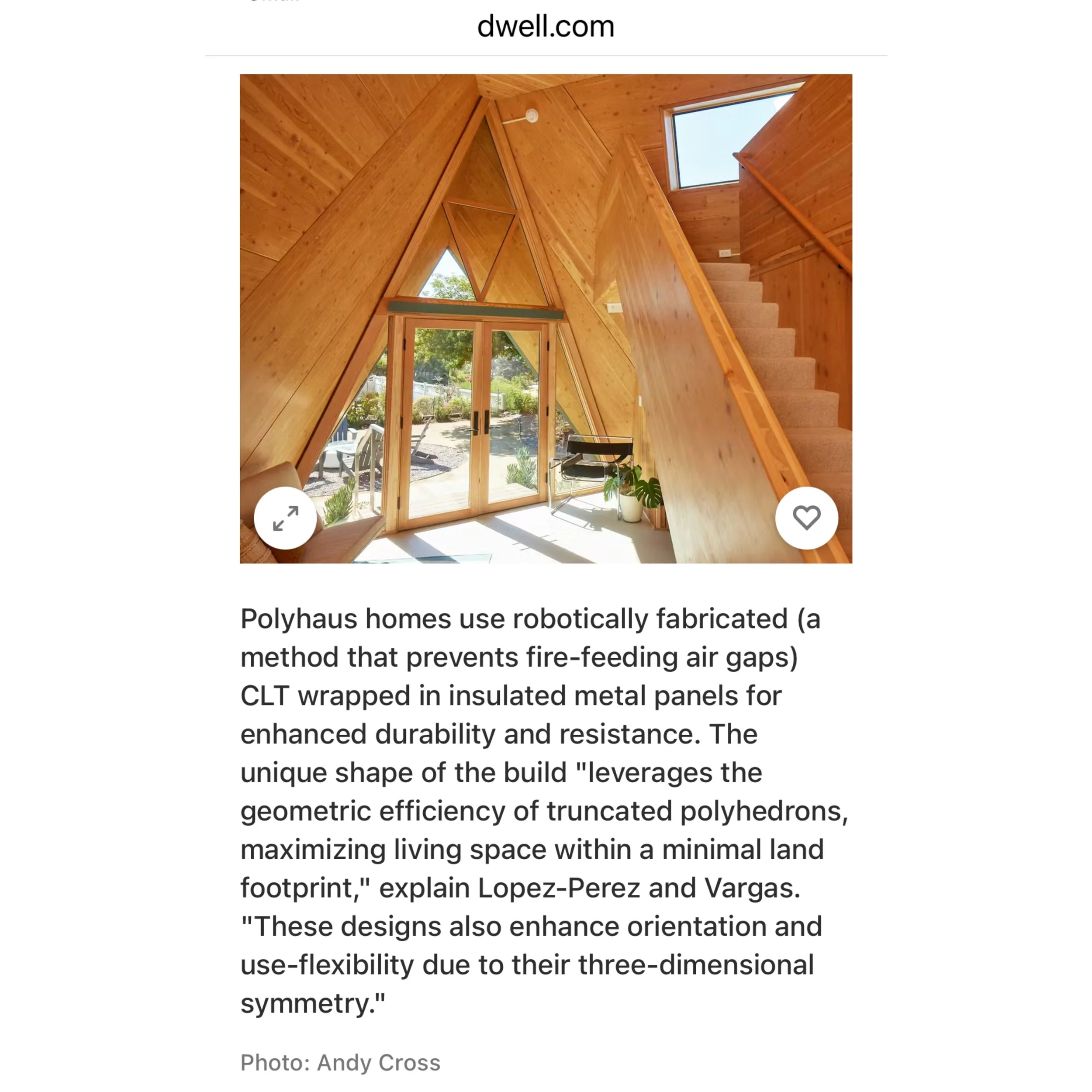 Interior view of a wooden A-frame house with large glass doors and windows, wooden staircase leading upstairs, and a seating area with plants, illuminated by natural sunlight.