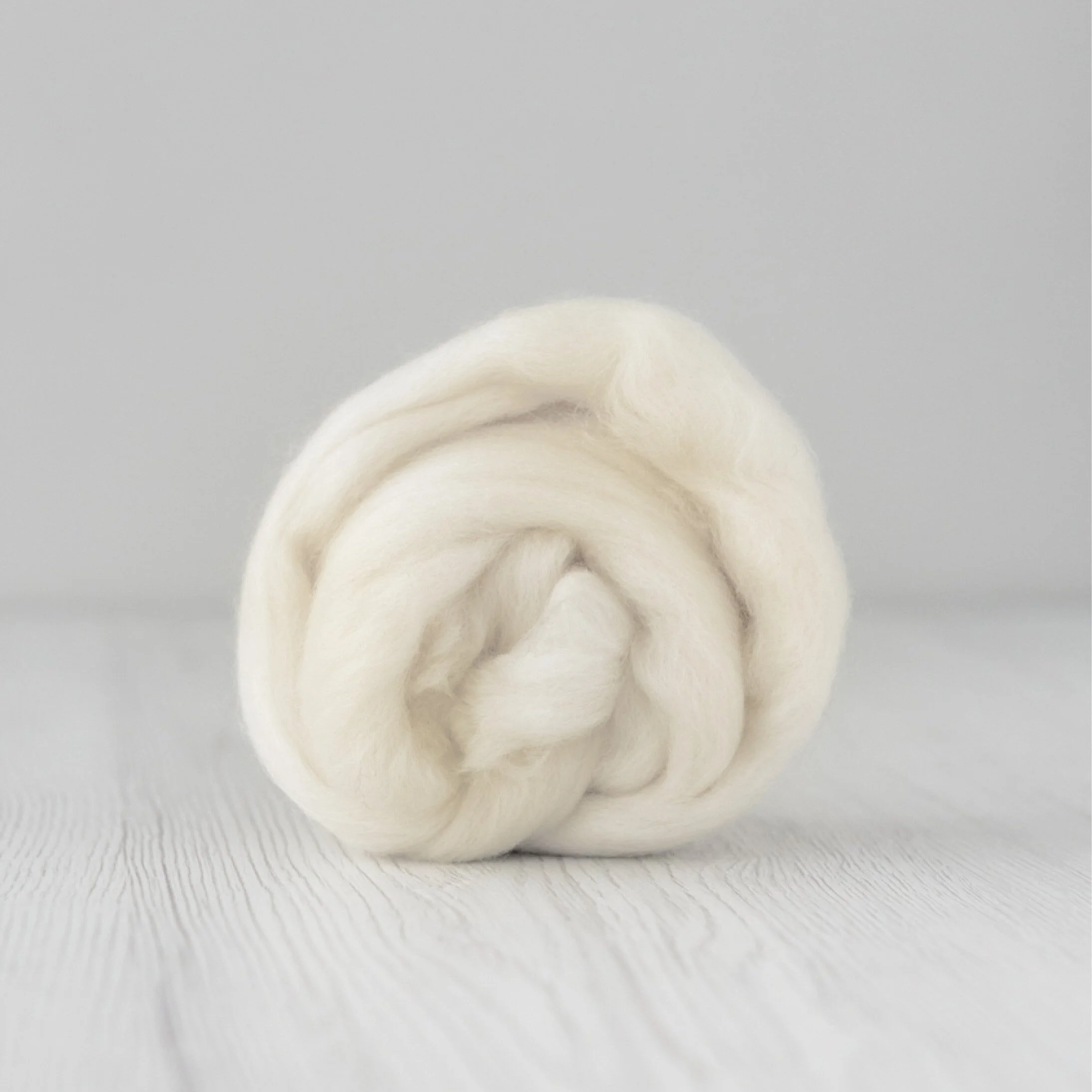 Close-up of a ball of white, soft, fluffy fiber or wool on a light-colored wooden surface with a plain background.