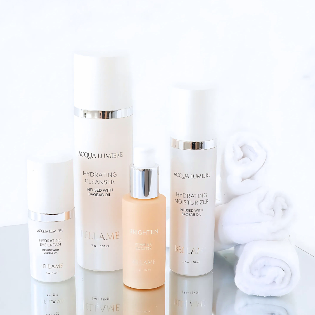 Collection of skincare products including a hydrating eye cream, hydrating cleanser, vitamin C booster, and hydrating moisturizer, with rolled white towels in the background.