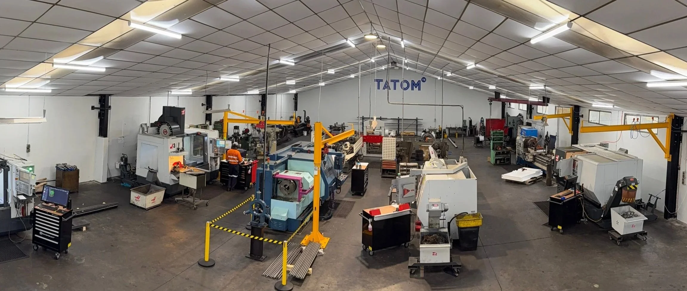 View of an industrial workshop with various manufacturing machines, workers, and equipment inside a spacious warehouse.
