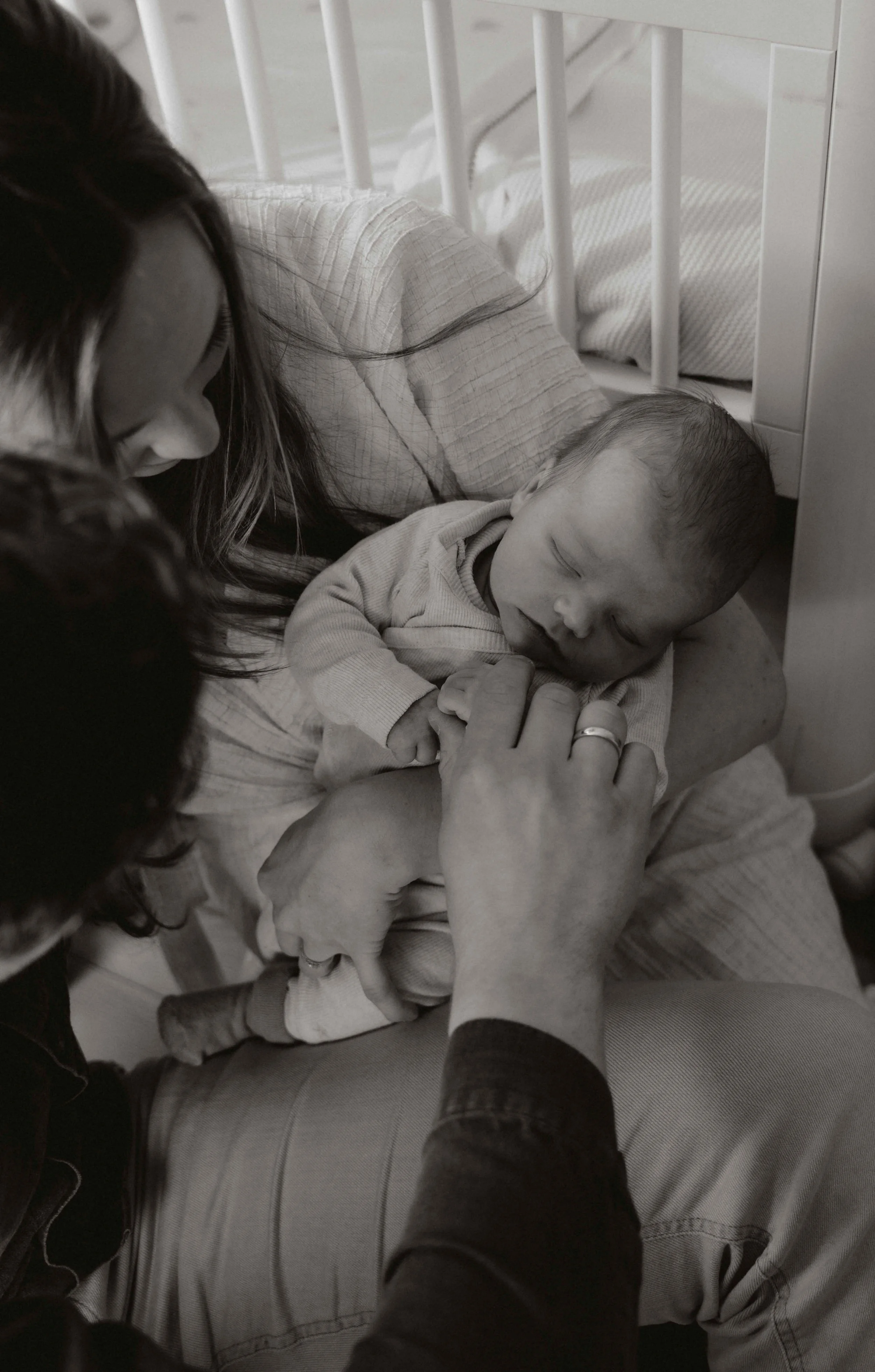 Zwart-witfoto van een baby die op een schoot ligt, omringd door volwassenen die het koesteren en verzorgen.