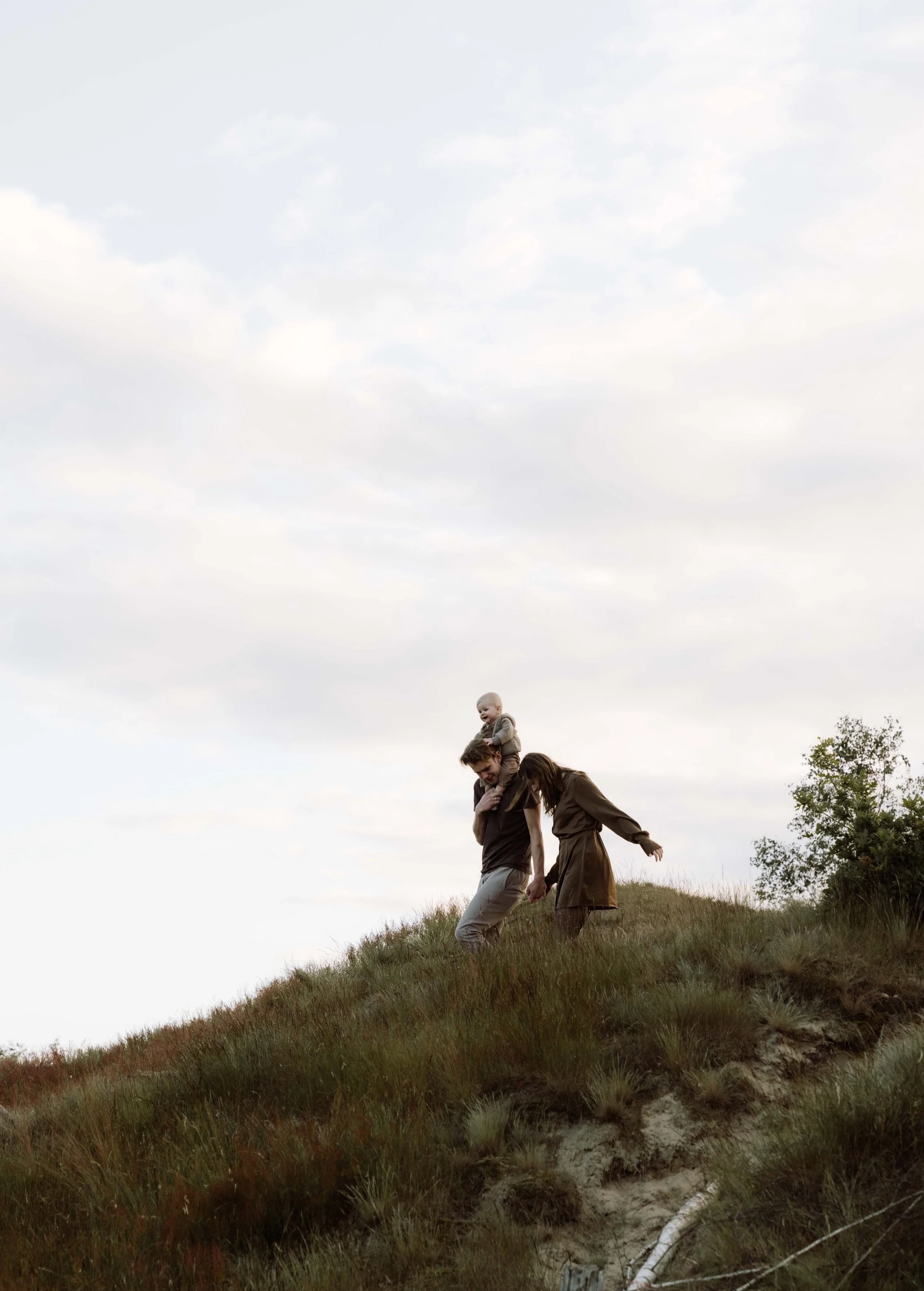 Een gezin met een man, een vrouw en een kind op een heuvel met gras, onder een bewolkte hemel.