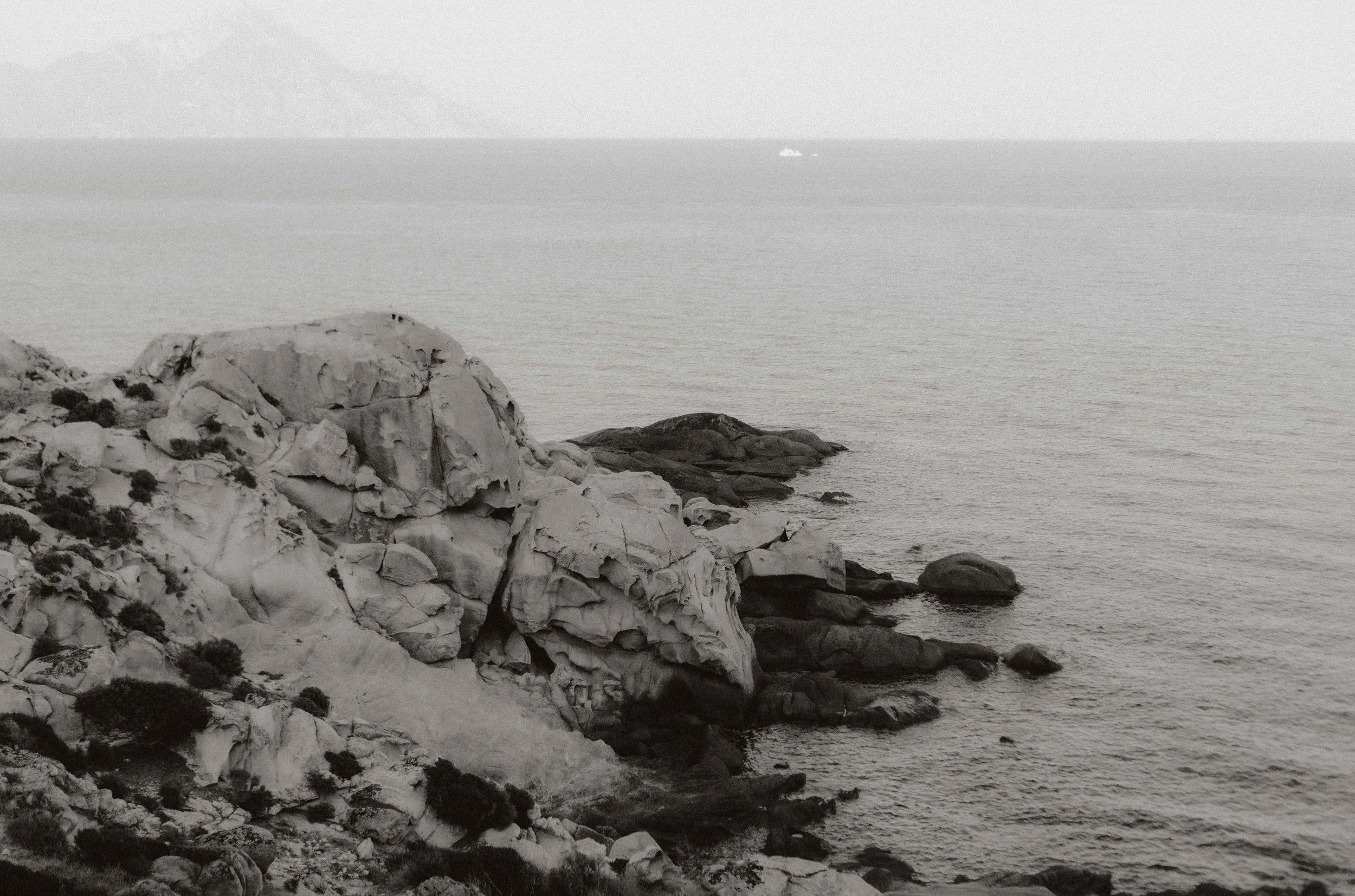 Zeegezicht met rotsformaties en een boot op de achtergrond, in zwart-wit.
