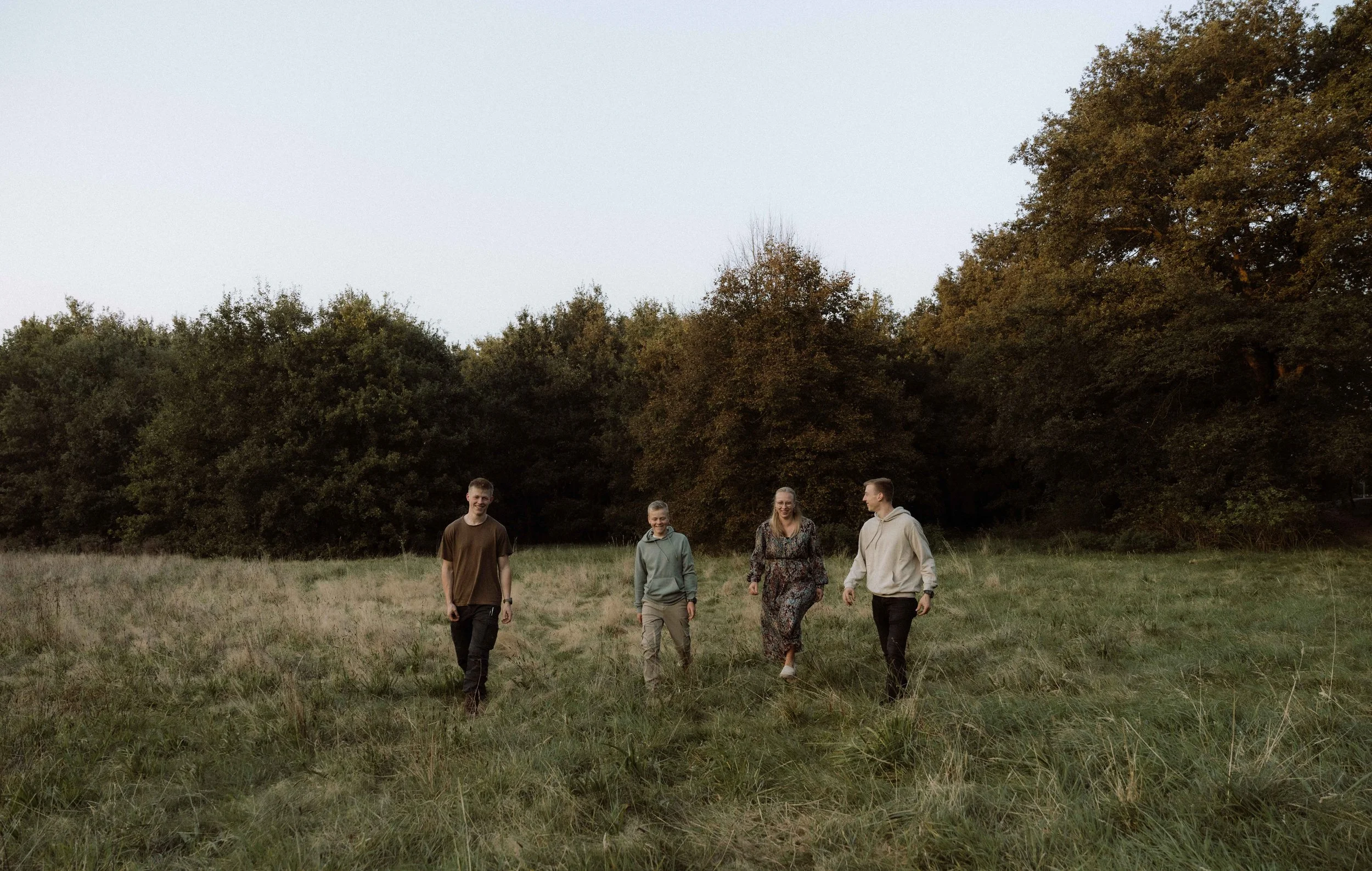 Vier mensen wandelen door een grasveld met bomen op de achtergrond tijdens de schemering.