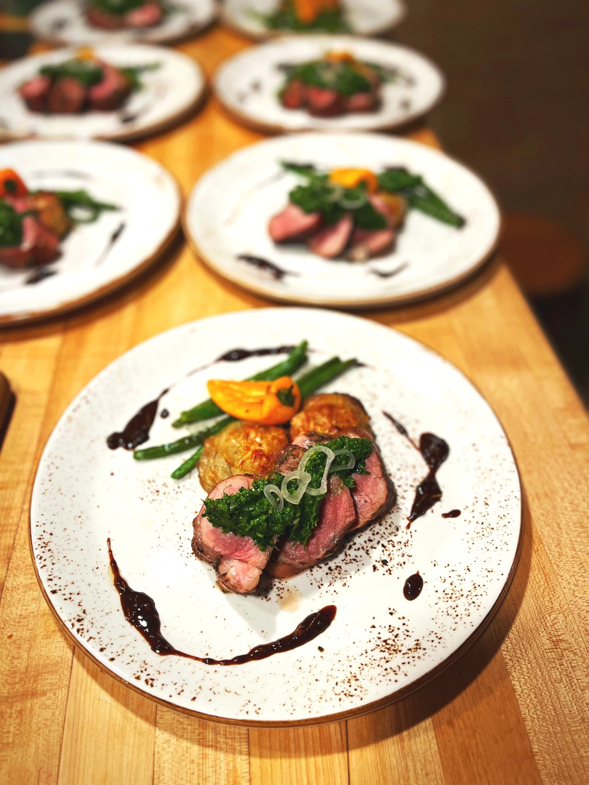 Plate of sliced steak with green beans, roasted potatoes, and a sauce drizzle on a wooden table.