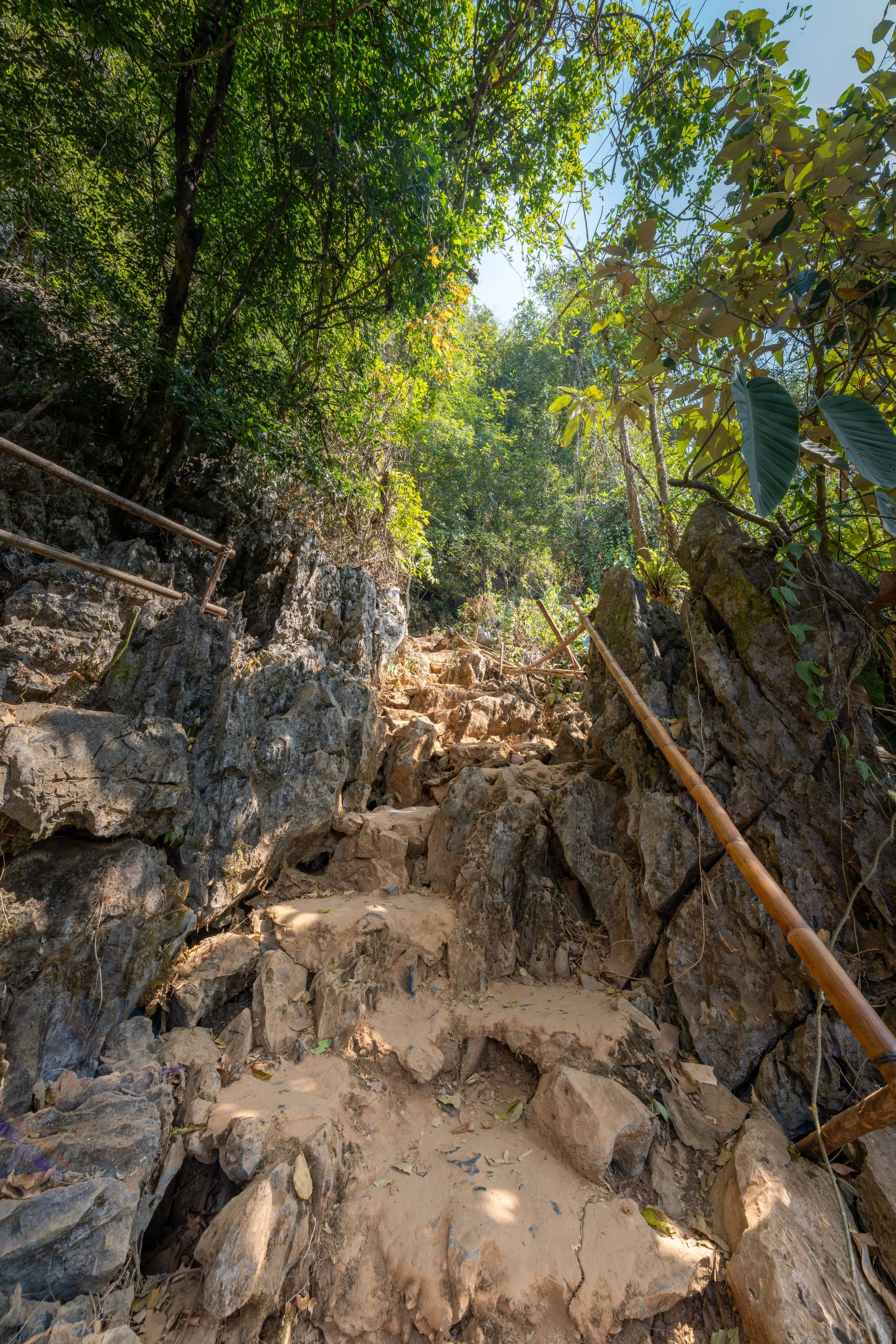 Der Aufstieg zur Tham Poukham Höhle führt über einen steilen Pfad durch die Karstlandschaft und belohnt mit eindrucksvollen Ausblicken auf die umliegenden Berge und Täler.