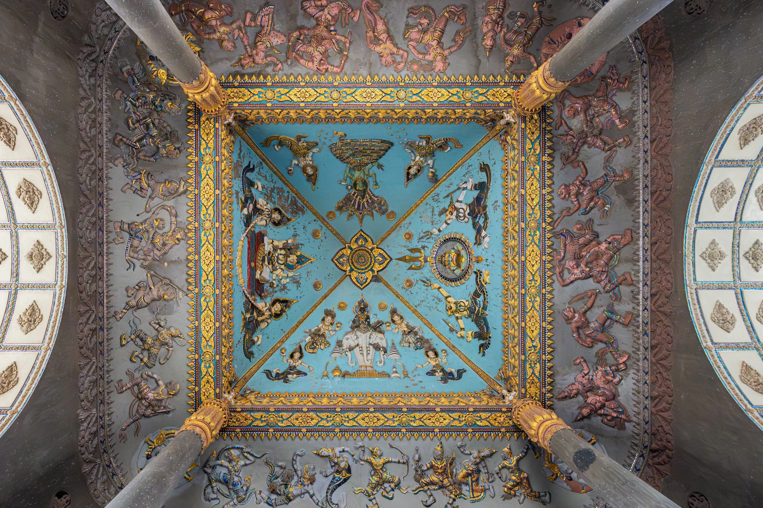 Das Deckenfresko im Patuxay ist reich mit farbenprächtigen Darstellungen himmlischer Wesen, Lotusblüten und mythologischer Symbole gestaltet, die im buddhistischen Verständnis Reinheit, Schutz und spirituelle Harmonie verkörpern. Dort ist auch der dr