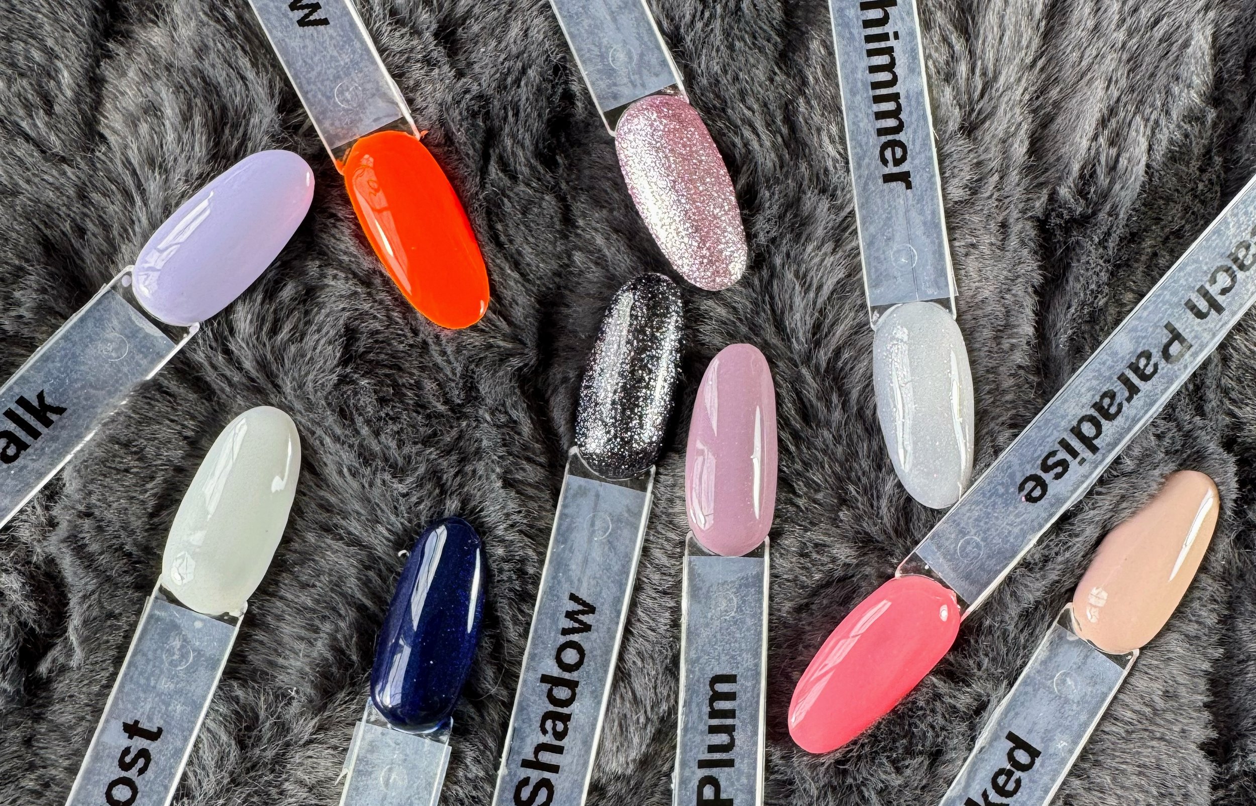 Zes flesjes nagellak van Florence Beauty & Nails in verschillende kleuren op een zachte, grijze stoffen achtergrond.