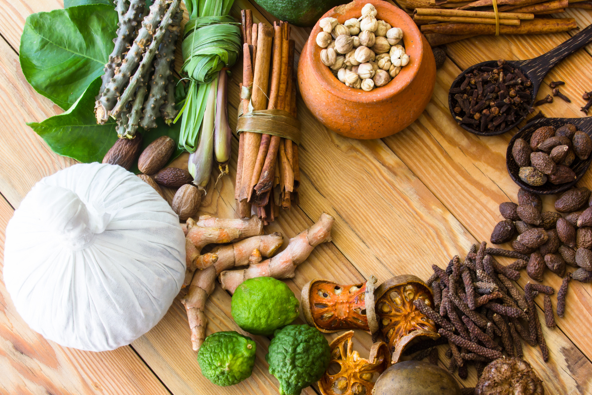 Ayurvedische Heilkräuter, Kurkuma, Zimtstangen und Kräuterstempel auf einem Holzuntergrund arrangiert.